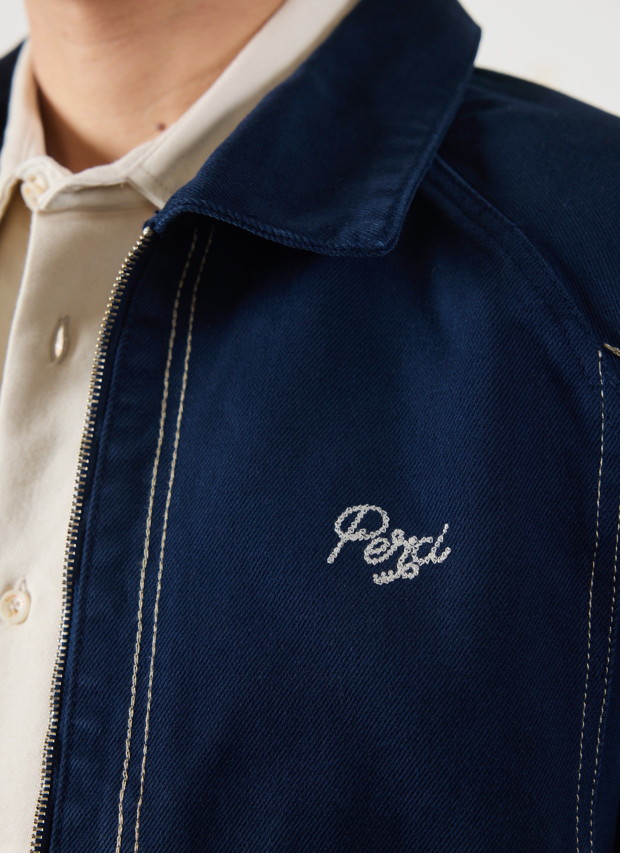 A close-up of the Percival Calabria Harrington Jacket in navy, detailing the contrast stitching and 'Perci' chest logo.