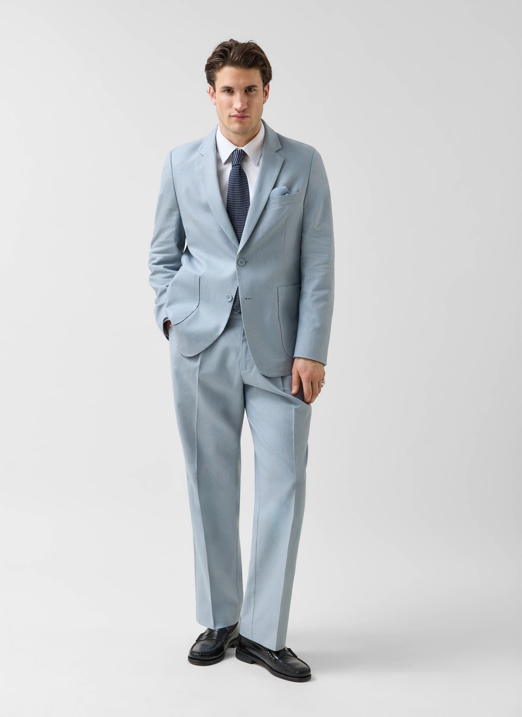 A man models the Percival light blue tailored linen blazer with matching trousers, a white shirt and a navy tie.