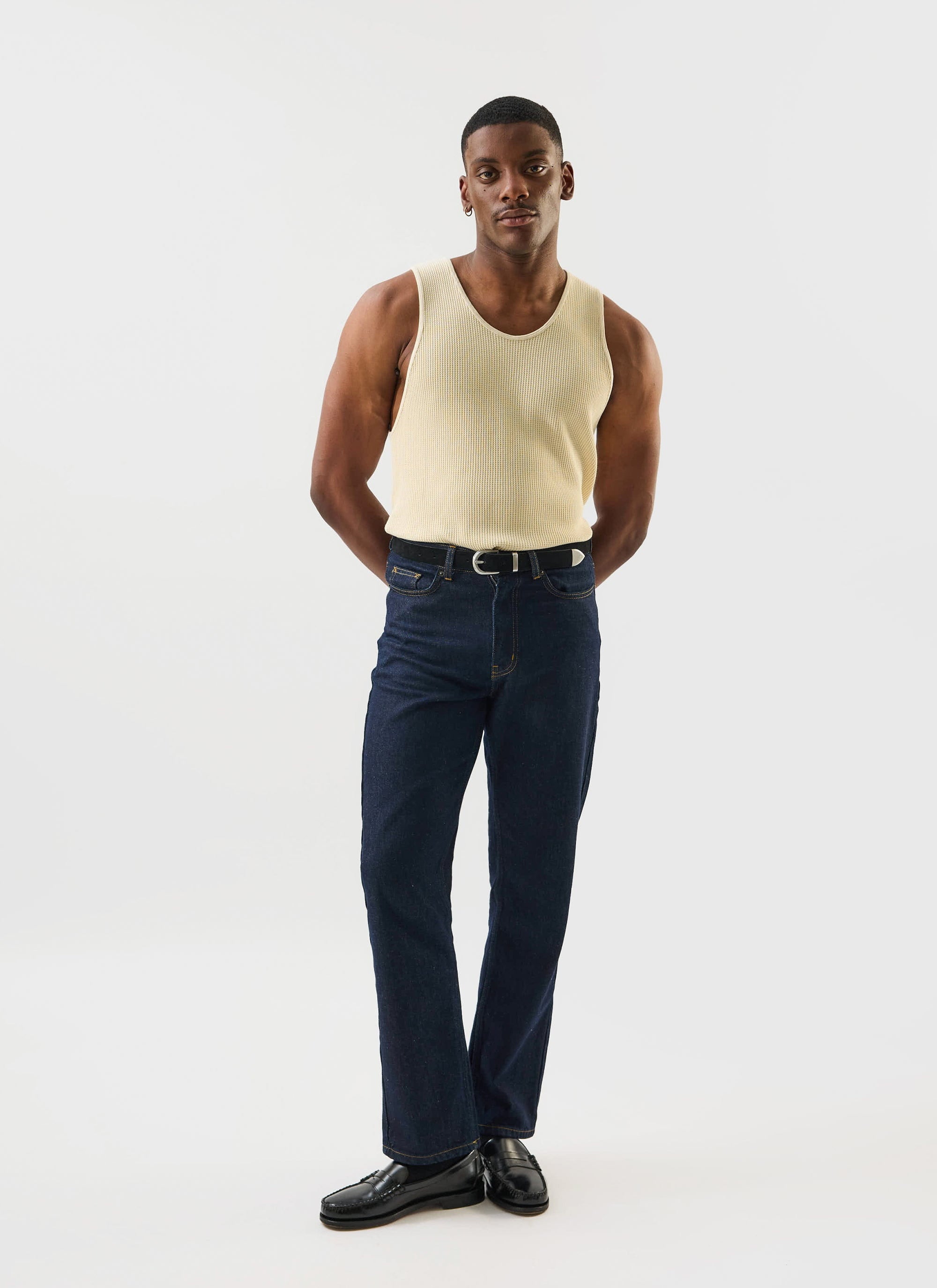 A full length shot of a model wearing the Percival Cotton Waffle Vest in ecru with dark denim jeans.
