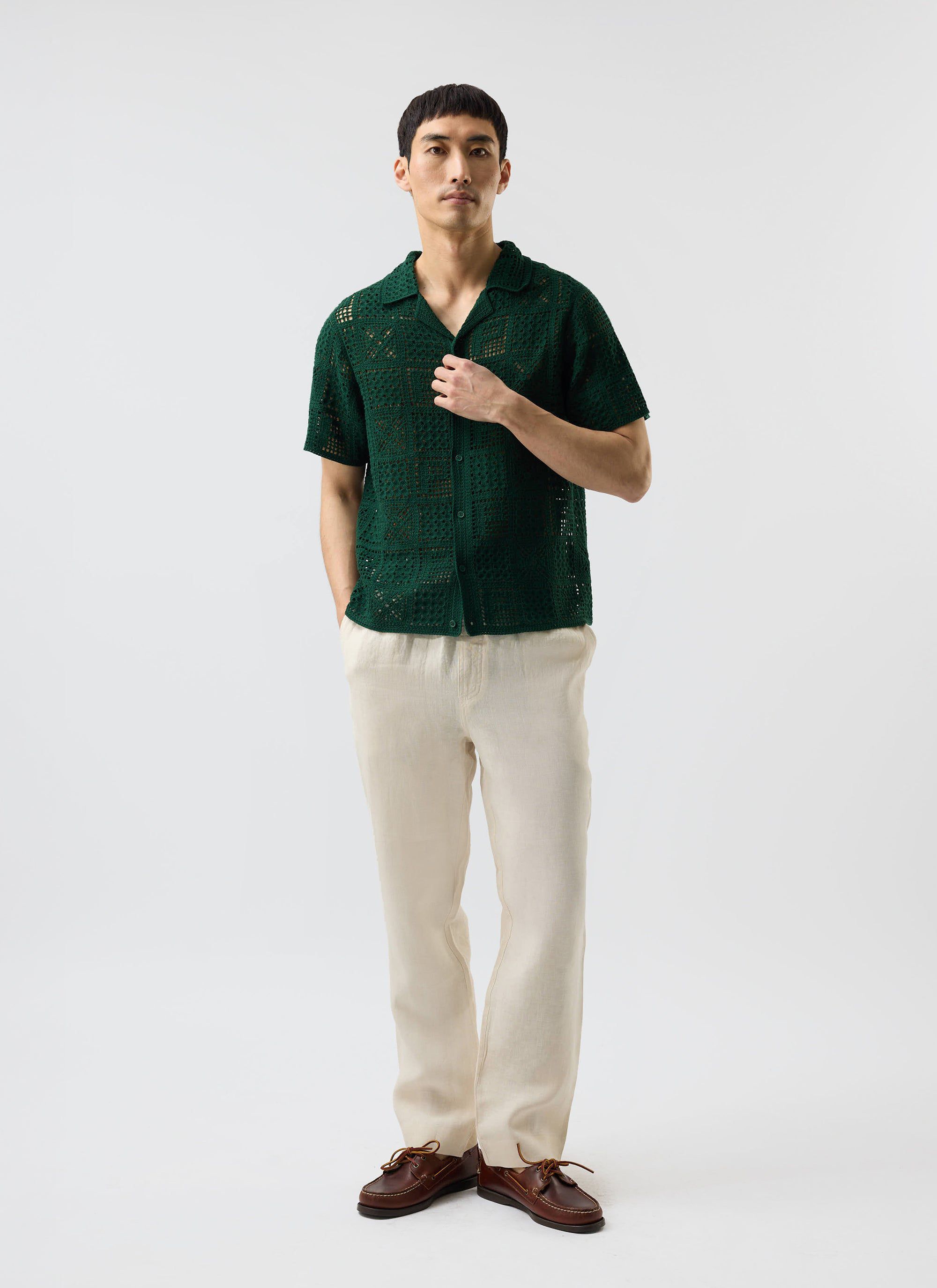 A model styles the Percival Crochet Groundsman Shirt in forest green, paired with cream linen trousers and brown boat shoes.