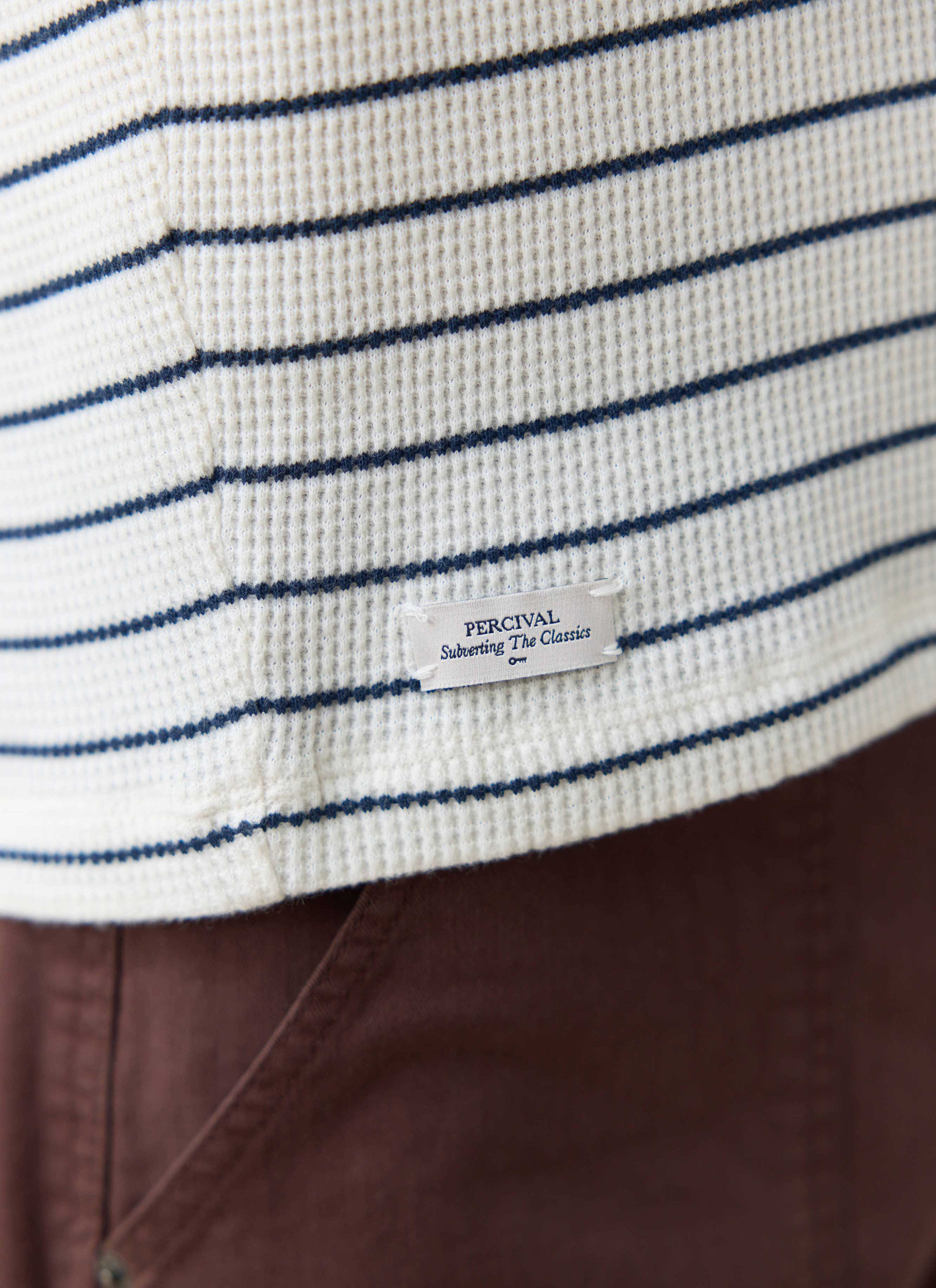 Close-up of the Percival side label on the cream and navy stripe Ernie Waffle T-Shirt in textured organic cotton.