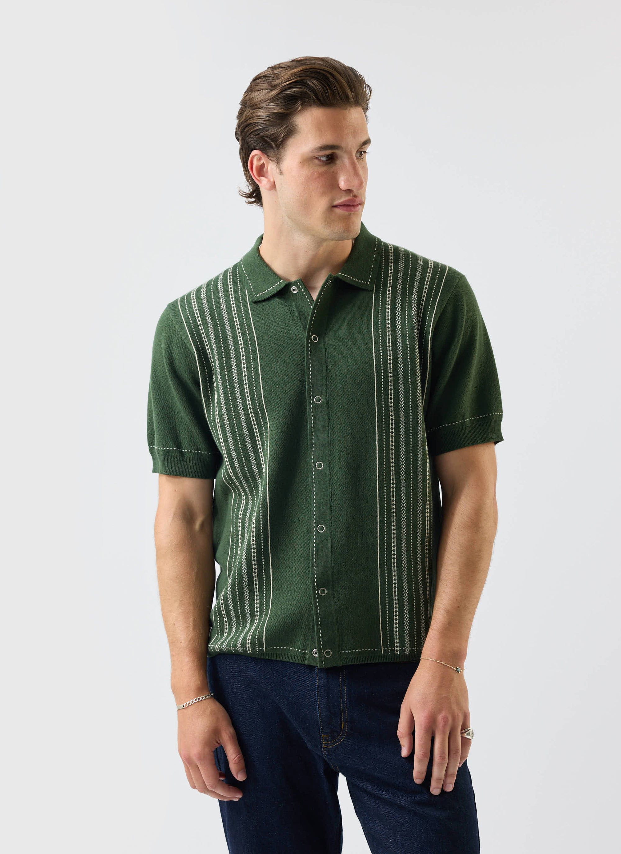 A model wears the Percival Accolades Knitted Short Sleeve Shirt in forest green, featuring a white jacquard stripe design.