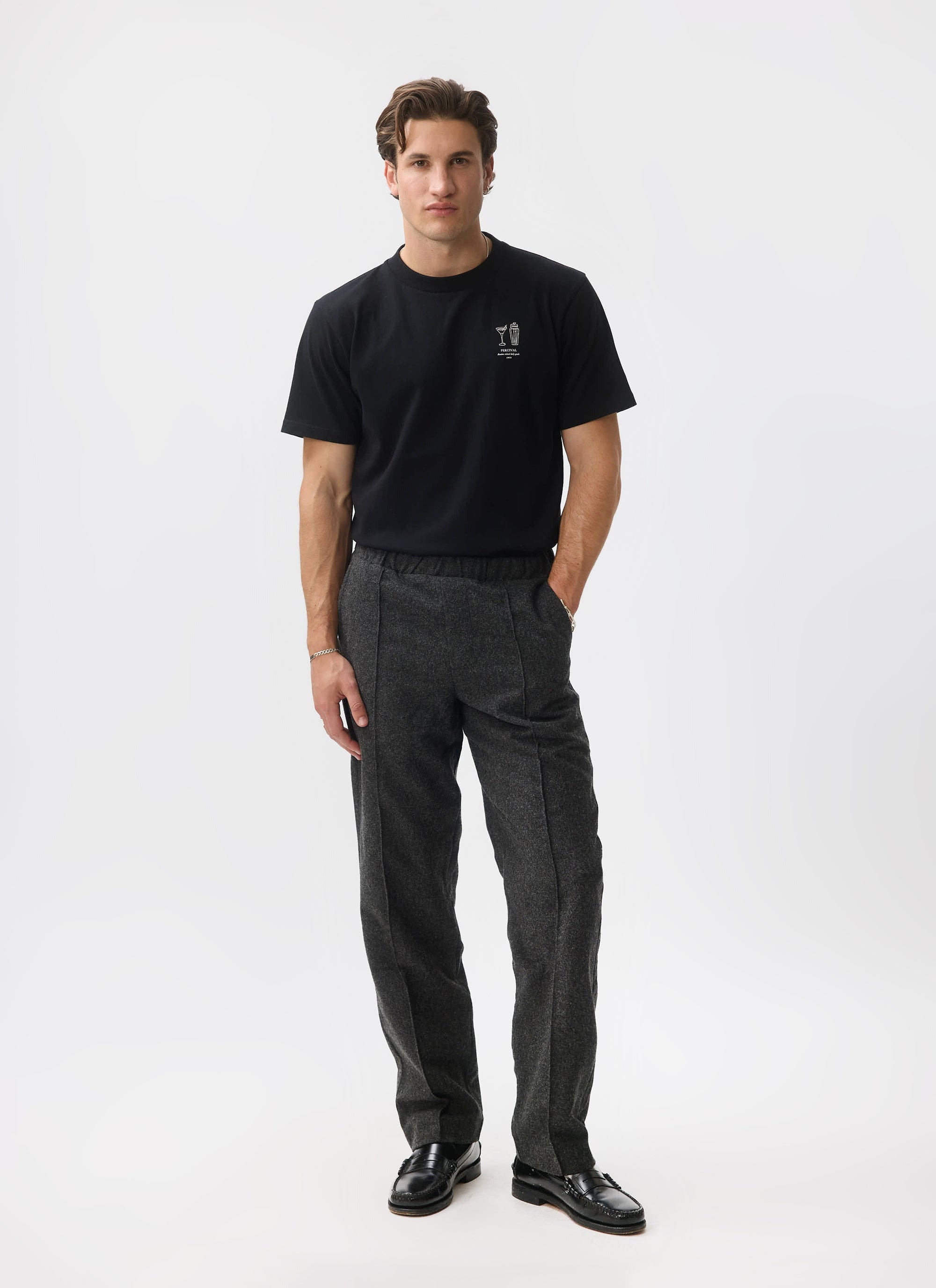 A model wears the Percival Caxton Smart Trousers in black brushed wool, styled with a black t-shirt and loafers.