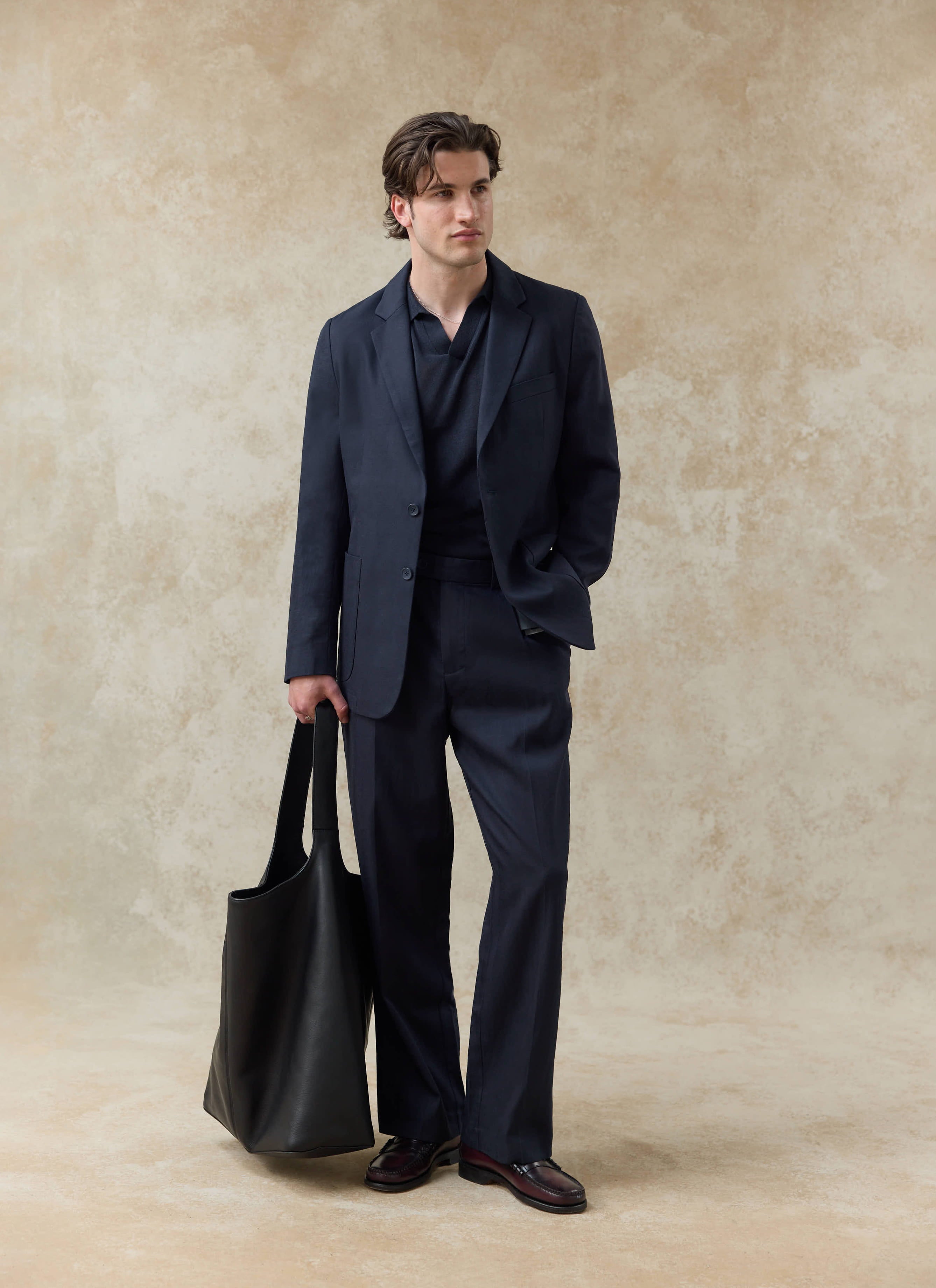 Navy Percival pleated lyocell trousers and matching blazer worn as a relaxed suit with a large black leather bag.