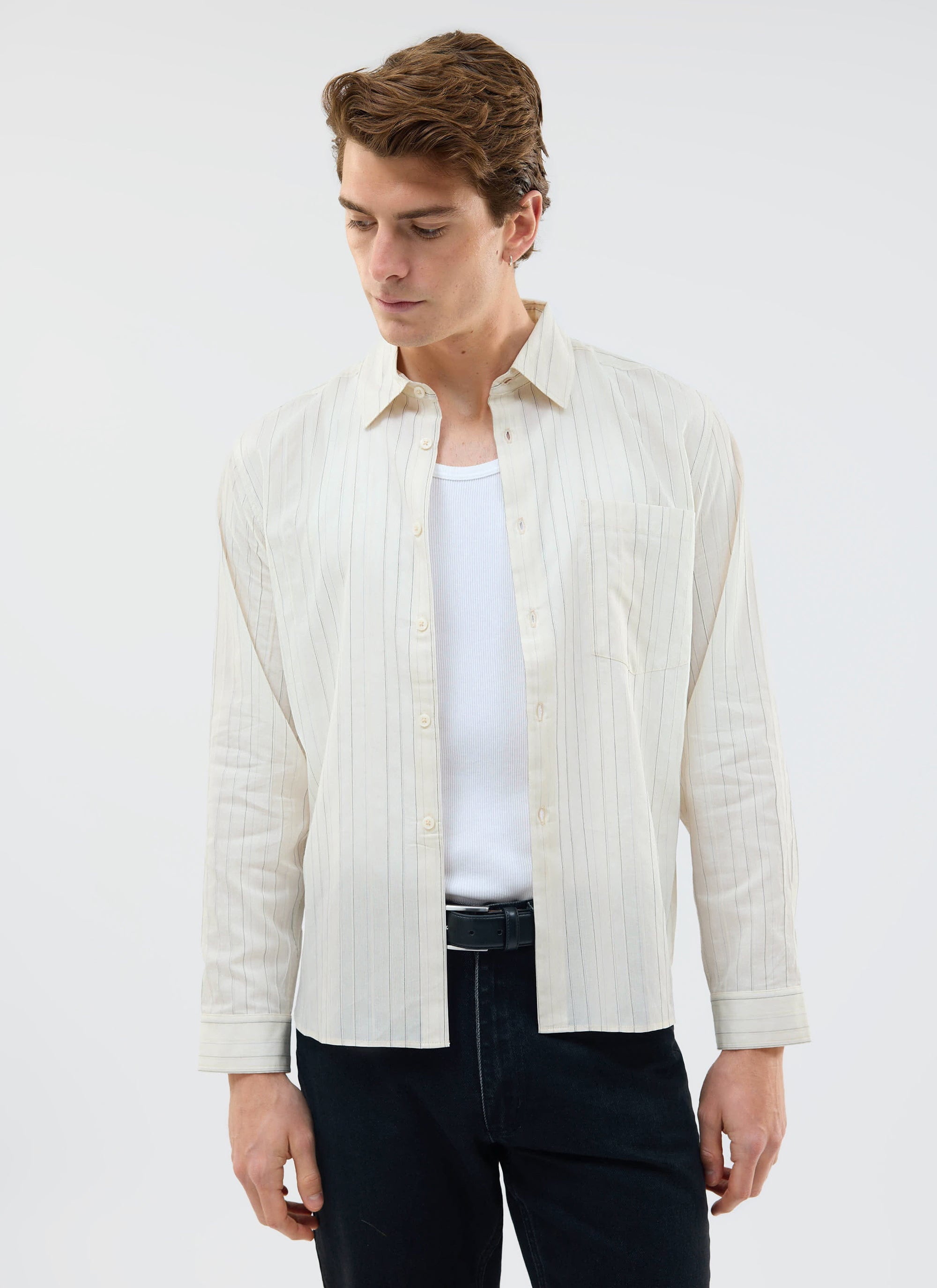 A model styles the ecru striped Lorenzo Pearce Shirt from Percival open over a white vest and black trousers.