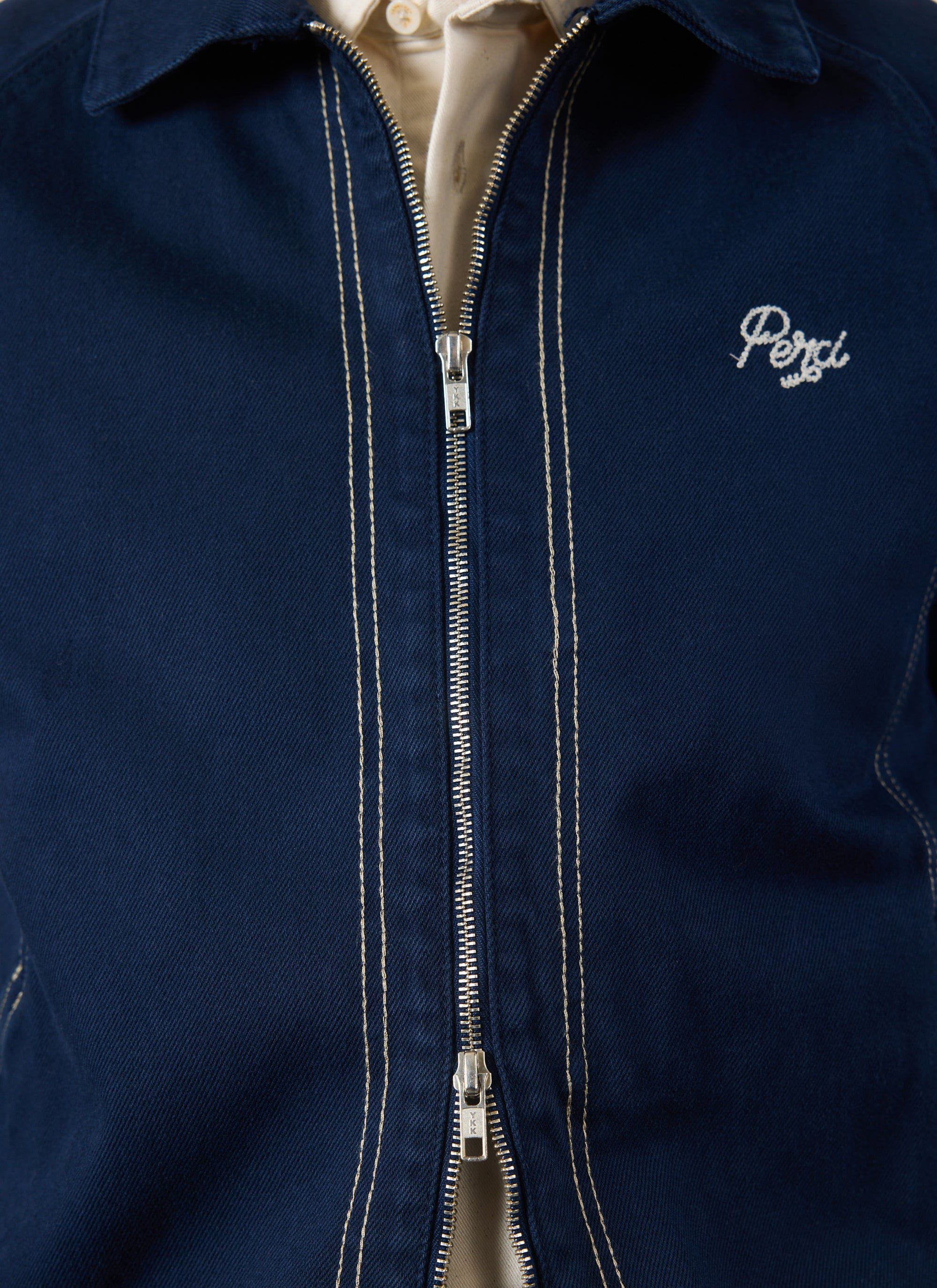A close-up of the navy Calabria Harrington Jacket by Percival, showing the zip, contrast stitching, and 'Perci' logo.