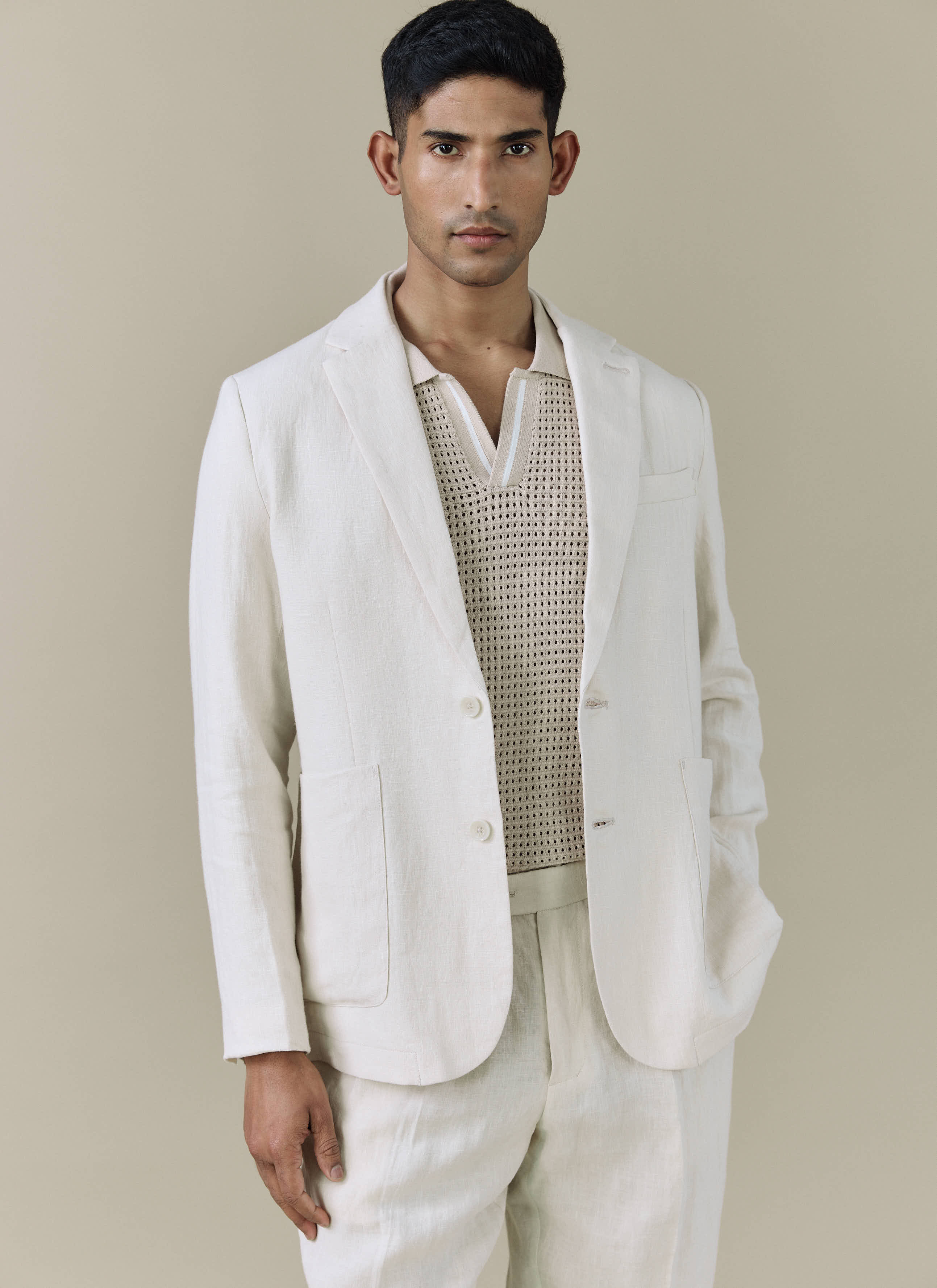 A model wears the Percival Tailored Linen Blazer in cream with matching trousers over a knitted polo shirt.