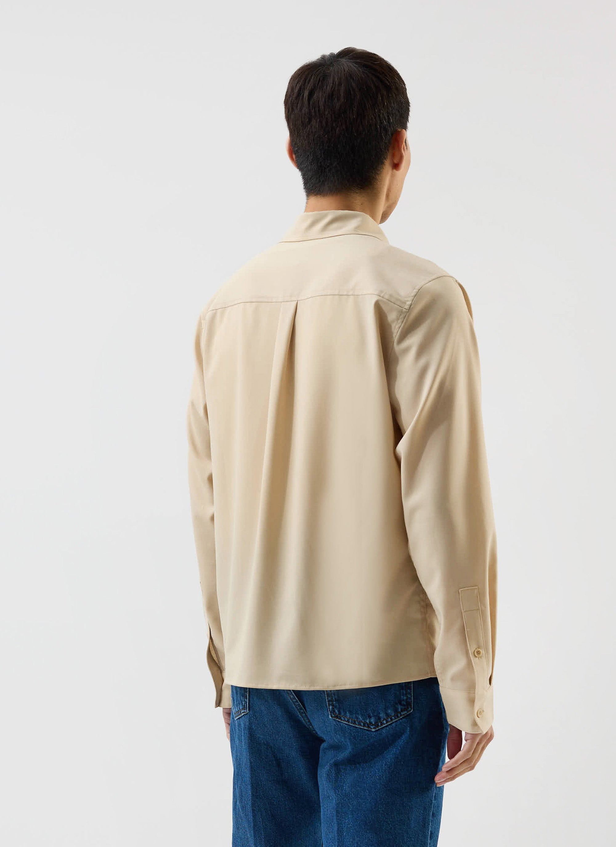 A rear view of a model wearing the Percival x Warren Safari Shirt in camel beige with blue jeans.