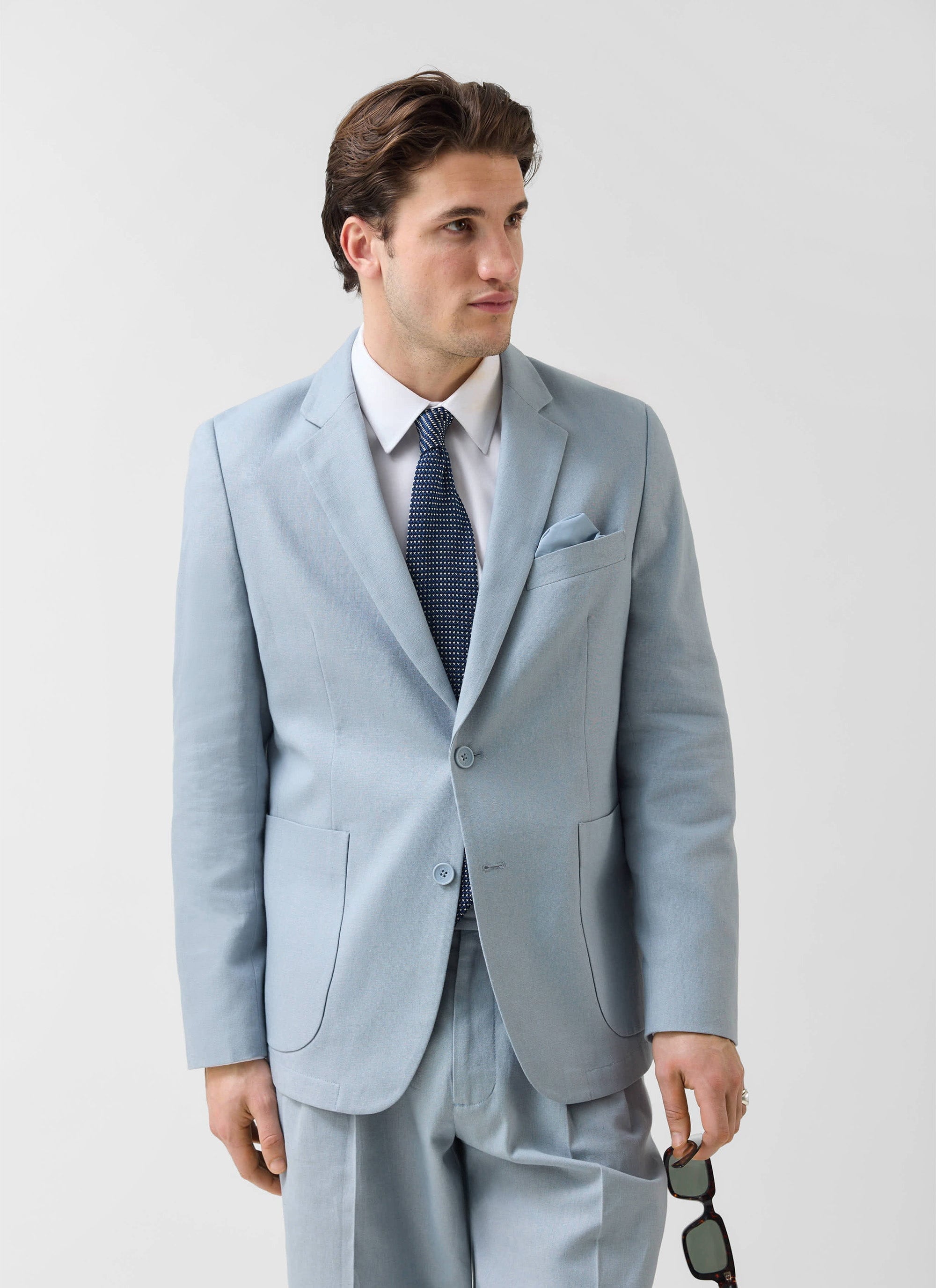A model wears the Percival light blue tailored linen blazer with a white shirt, tie and matching trousers.