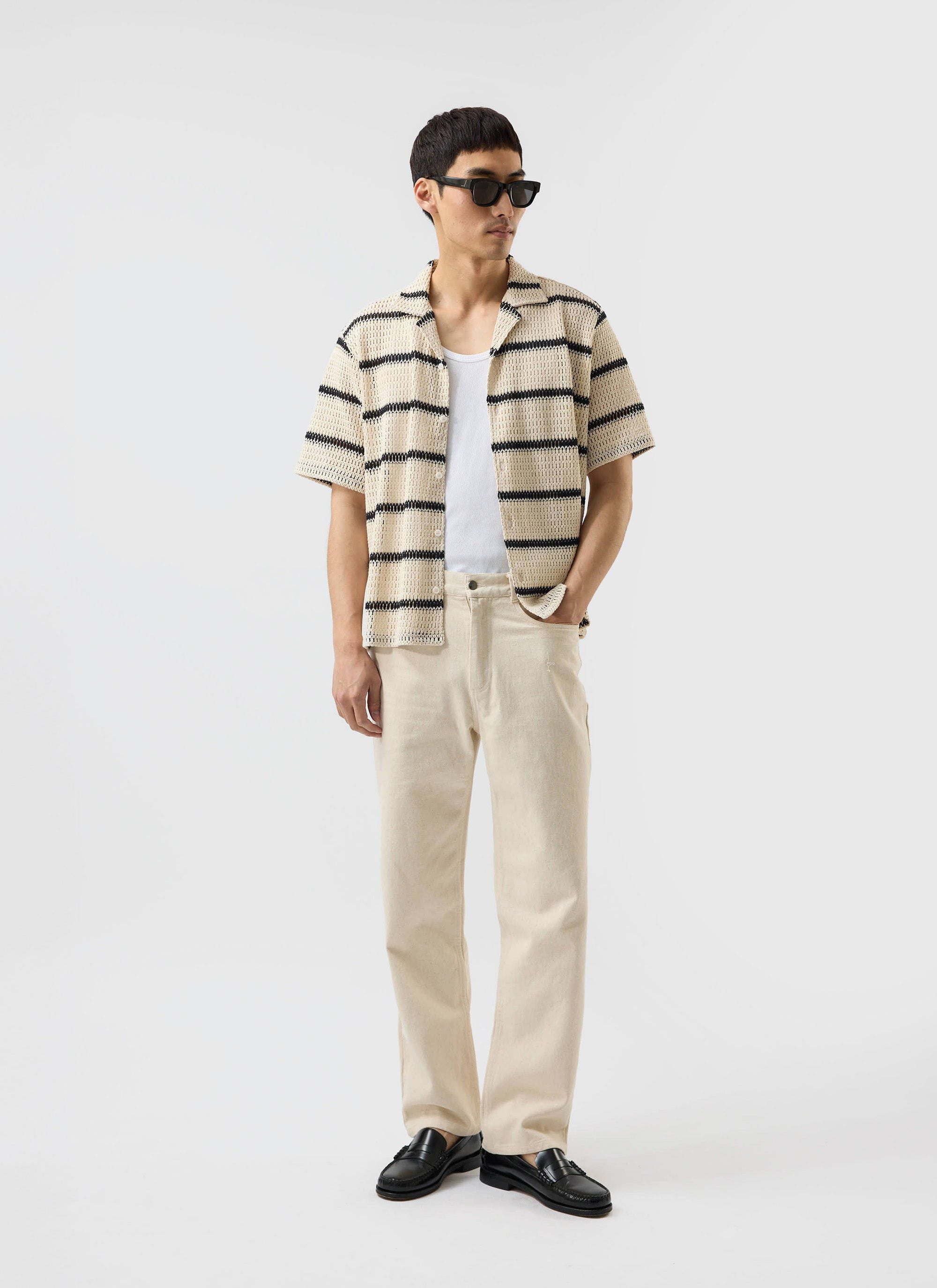 A model wears the Percival Crochet Groundsman Cuban Shirt in ecru with black stripes, styled open over a white vest.