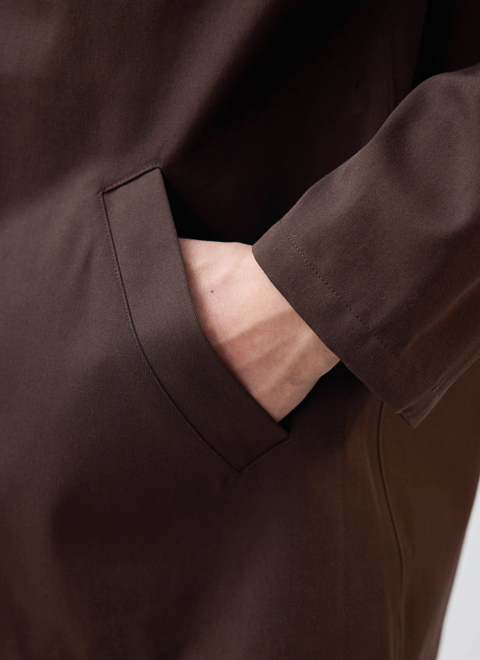 Close-up of a model's hand inside the welt pocket of the Percival Sherlock Short Trench Coat in Espresso.