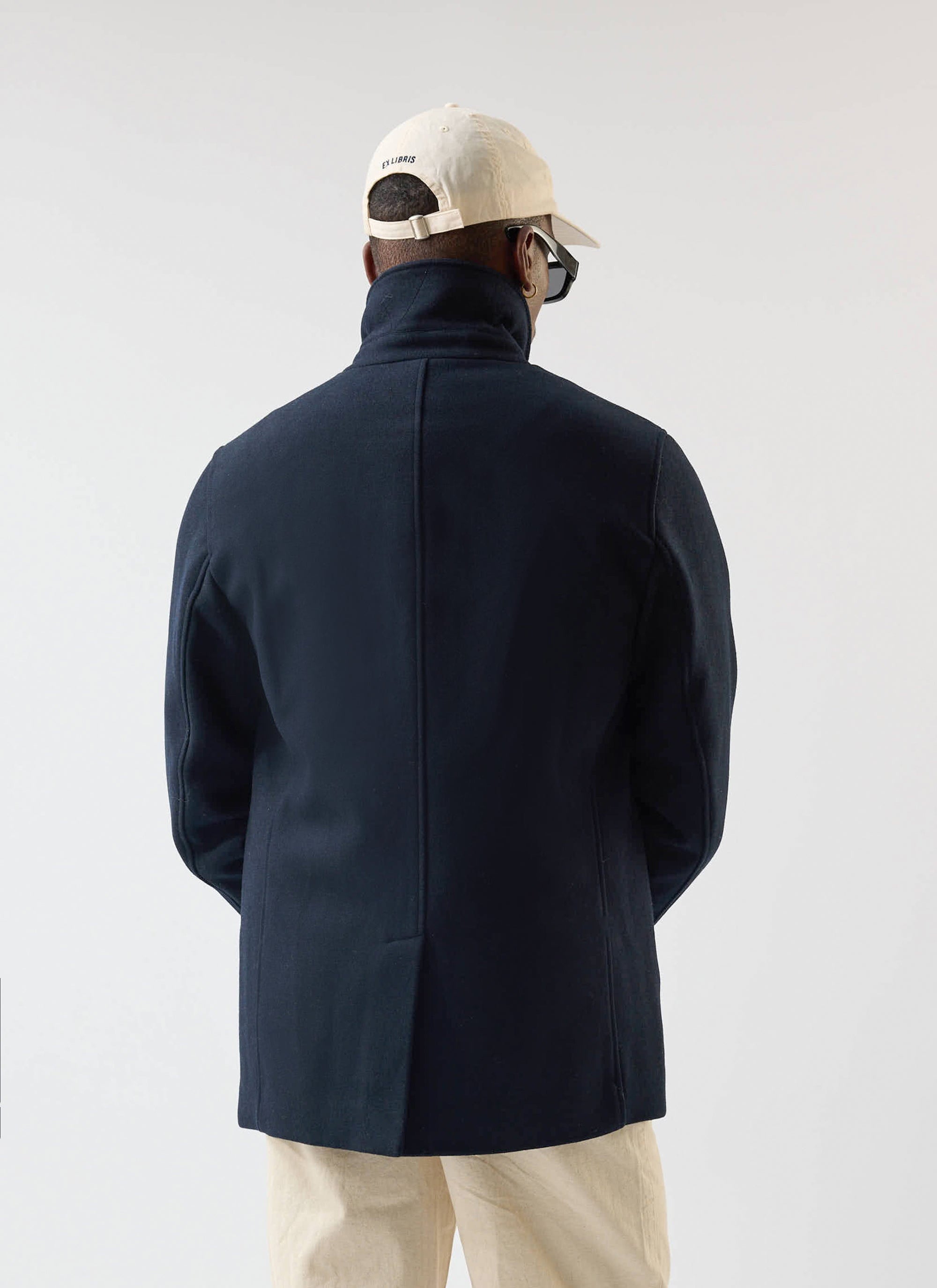 Back view of a model wearing the navy Melton Wool Peacoat from Percival, styled with a cream cap and trousers.