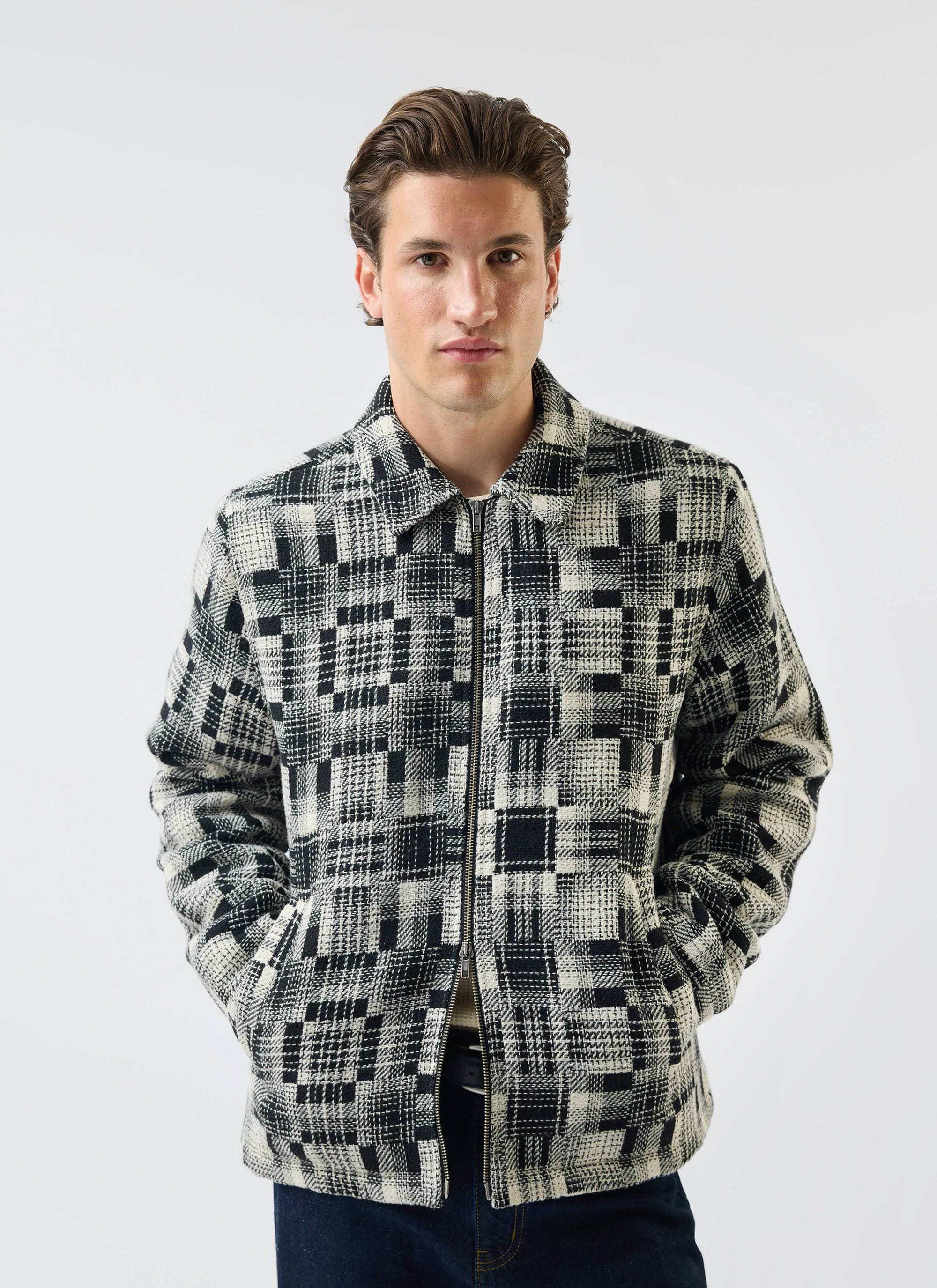 A model wears the Percival Glossary Patchwork Jacket in grey twill against a white studio background.