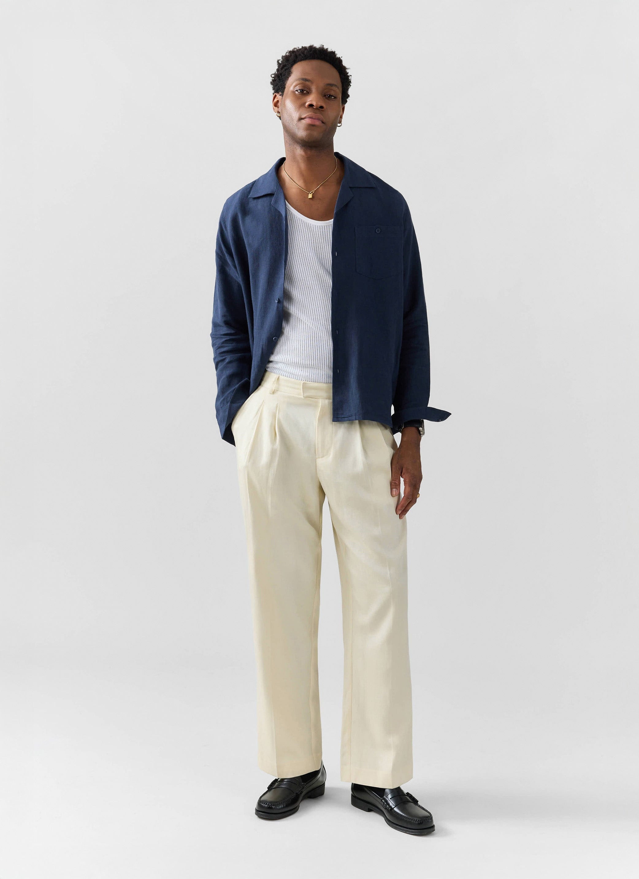 The Percival Long Sleeve Cuban Linen Shirt in navy, styled open on a model with a white vest and cream trousers.