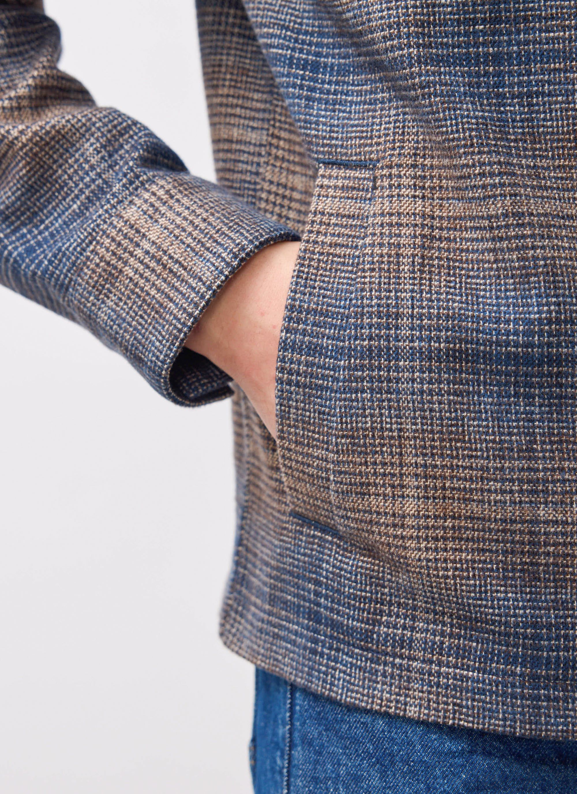 A close-up of a model's hand in the side welt pocket of the brown and blue Luton Check Overshirt from Percival.
