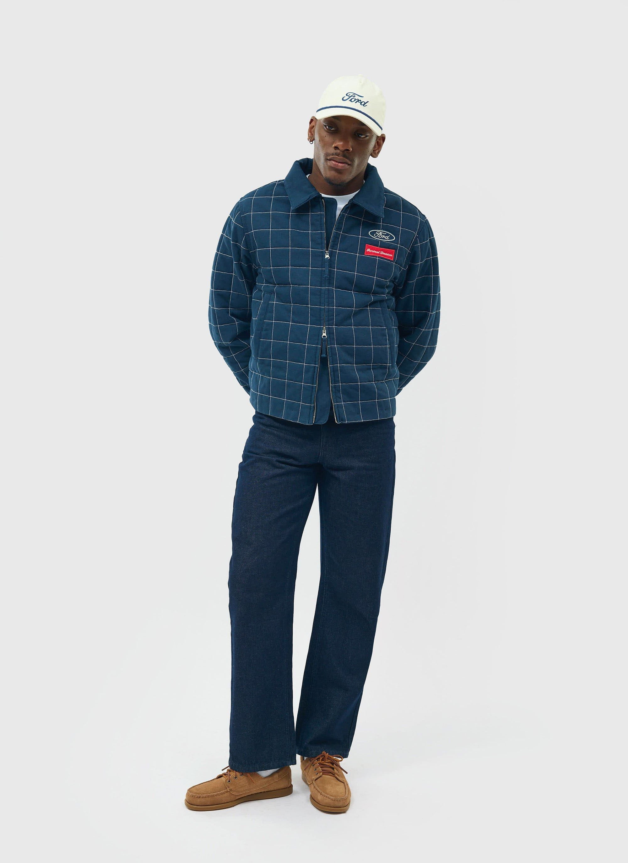 Model wears the navy Percival x Ford Garage Harrington Jacket, a quilted workwear style, with dark jeans and a white cap.