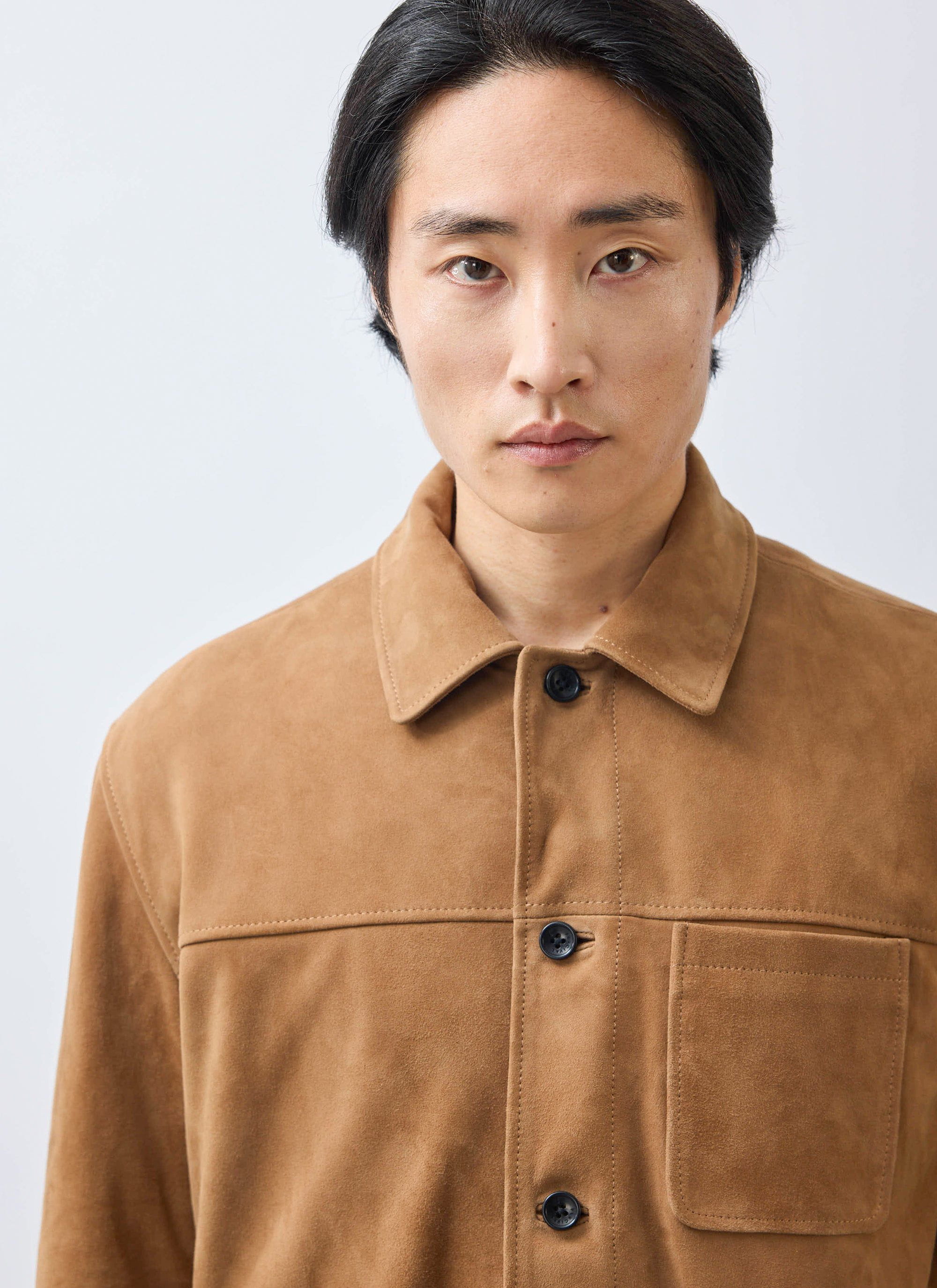 A close-up portrait of a model wearing the Percival Afterward Suede Chore Jacket in tan against a plain background.