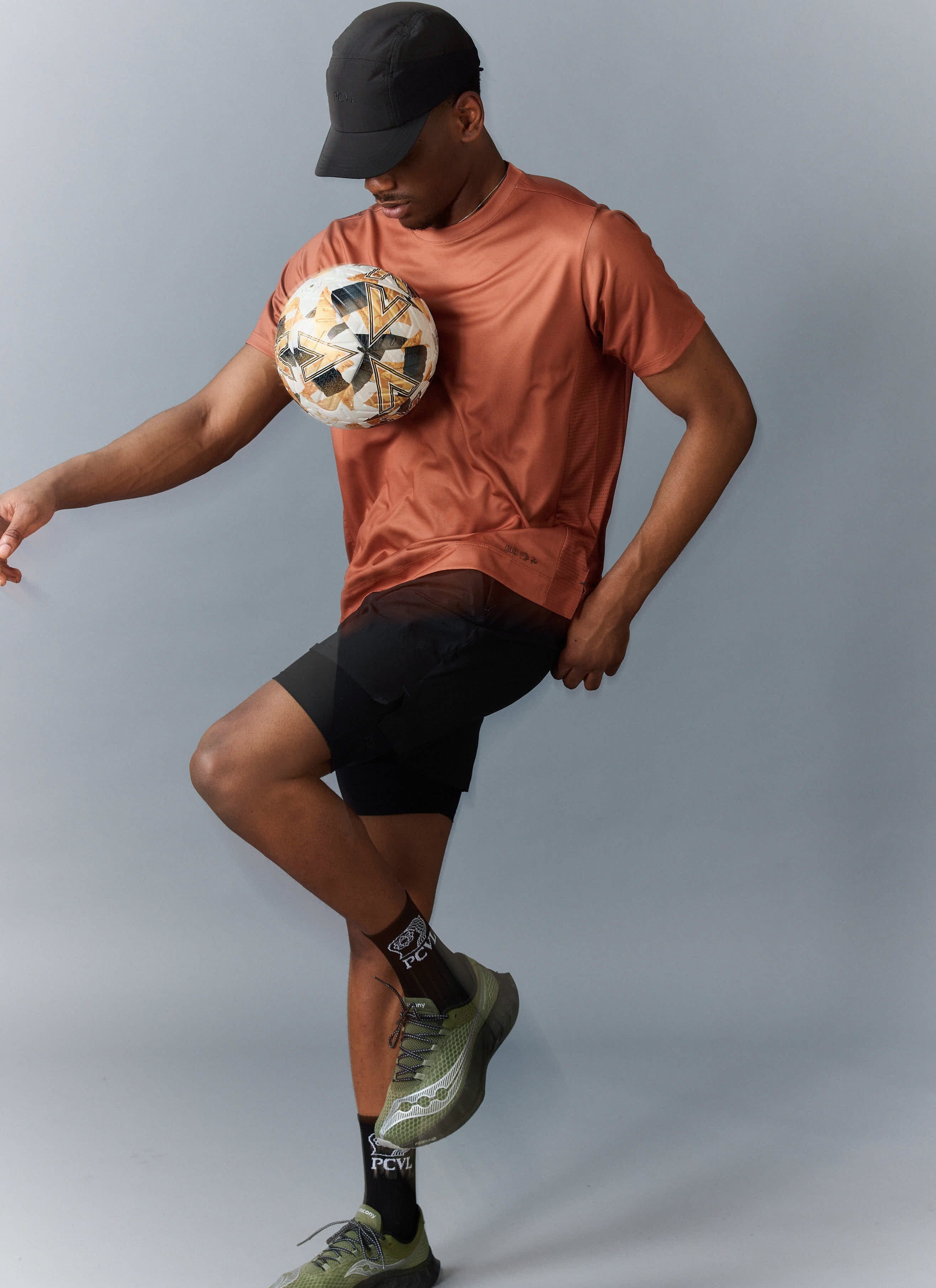 A man models the rust-coloured PCVL Performance Top from Percival, balancing a football on his chest.