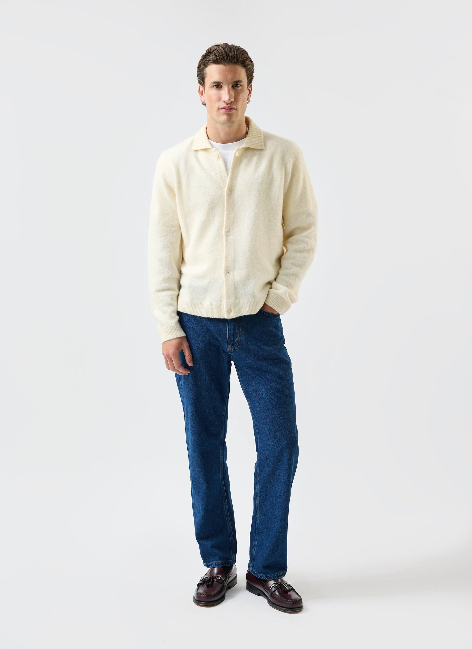 A man models the Percival Archive Wool Knitted Collared Cardigan in ecru cream with blue jeans and loafers.