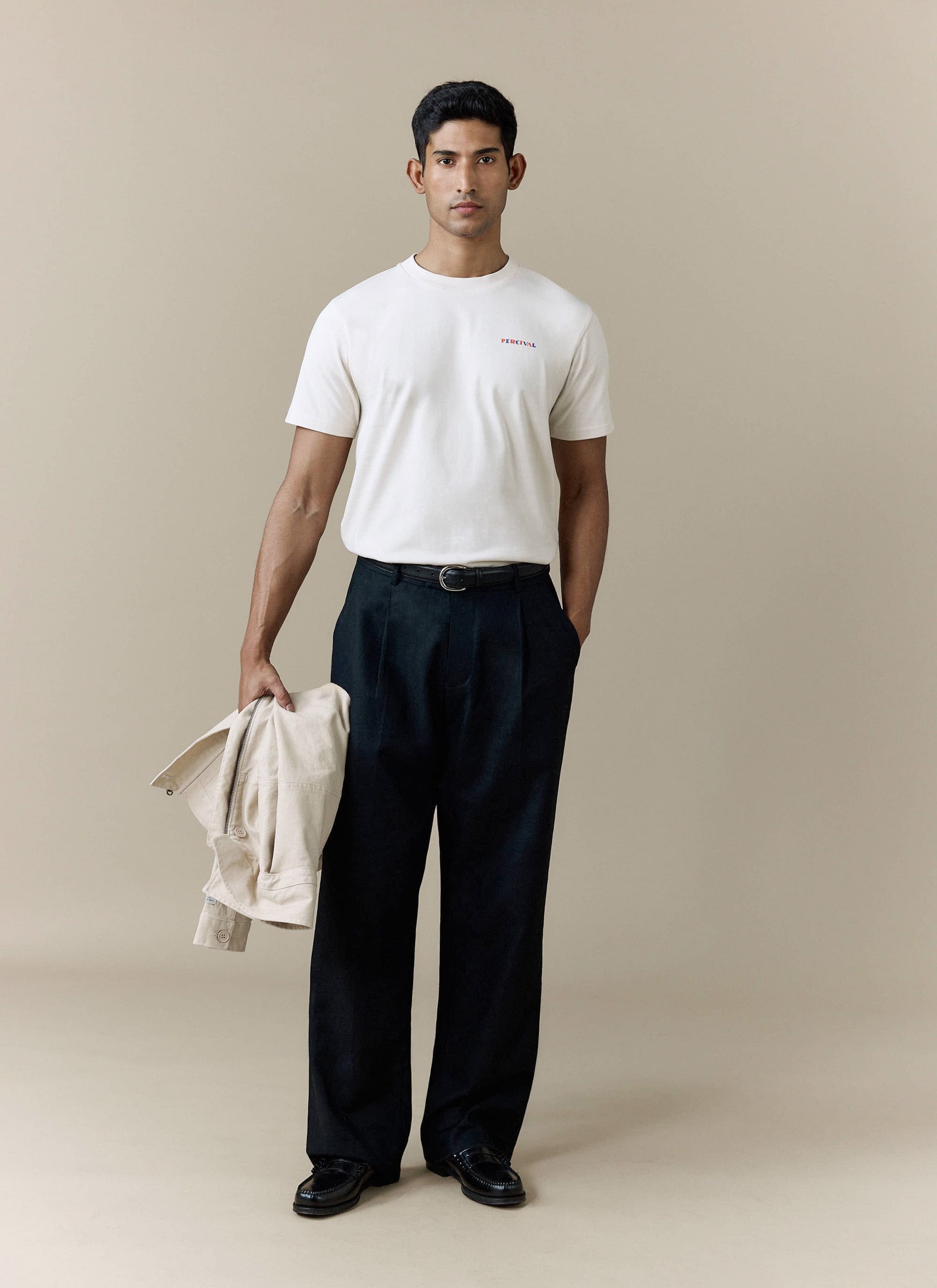 A model wears the Percival Mixologist Martini T-shirt in ecru, styled with smart black trousers and holding an ecru jacket.