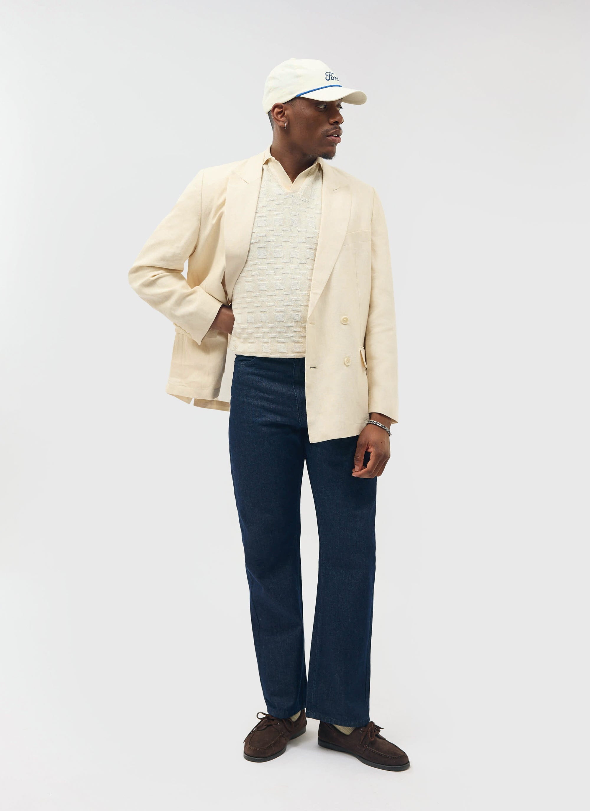 A model wears the Percival Deck Negroni Knitted Shirt in ecru, layered under a cream blazer and styled with dark denim.
