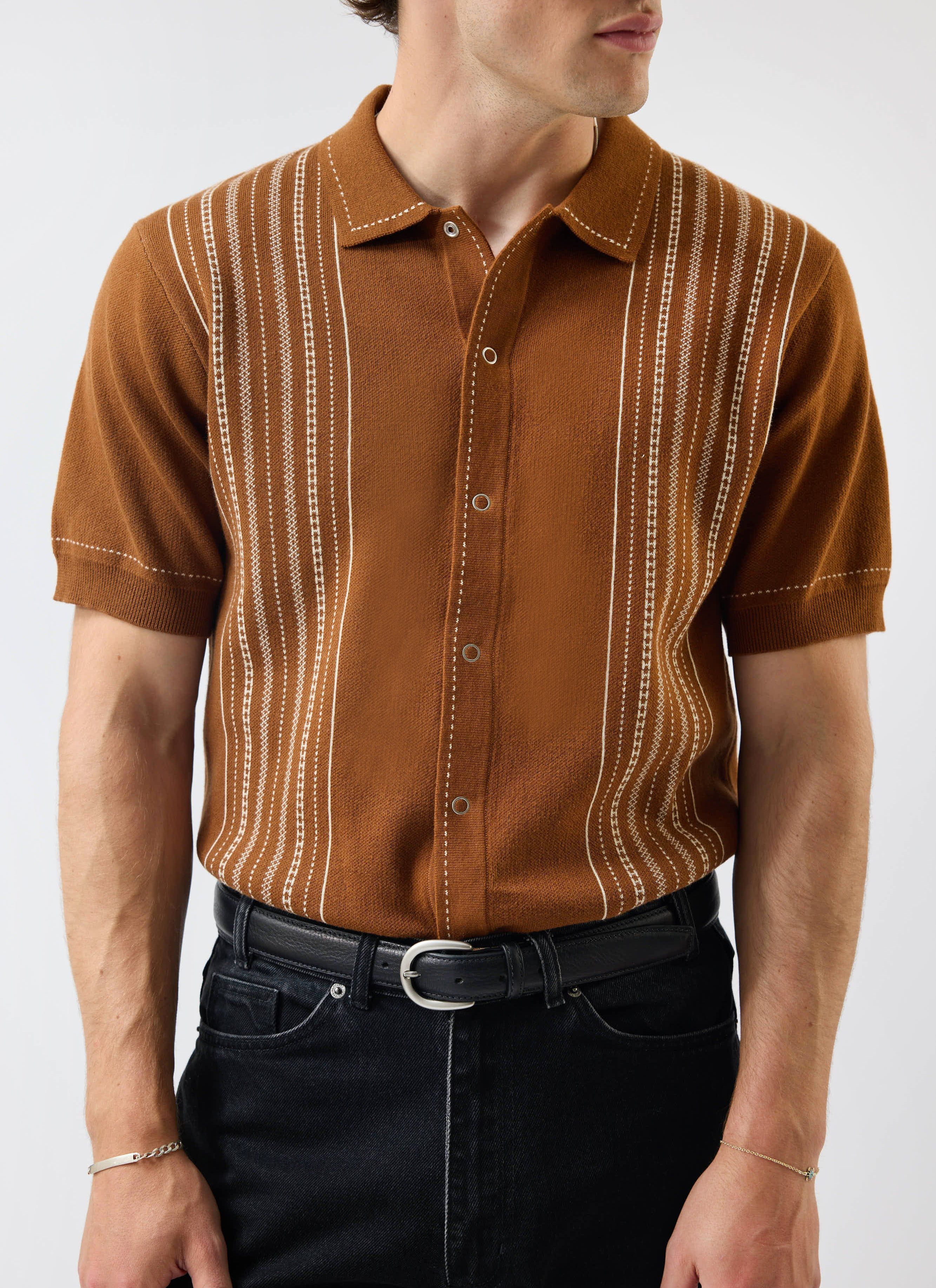 A man models the Percival Accolades Knitted Short Sleeve Shirt in Tobacco Brown, featuring a vertical white jacquard pattern.