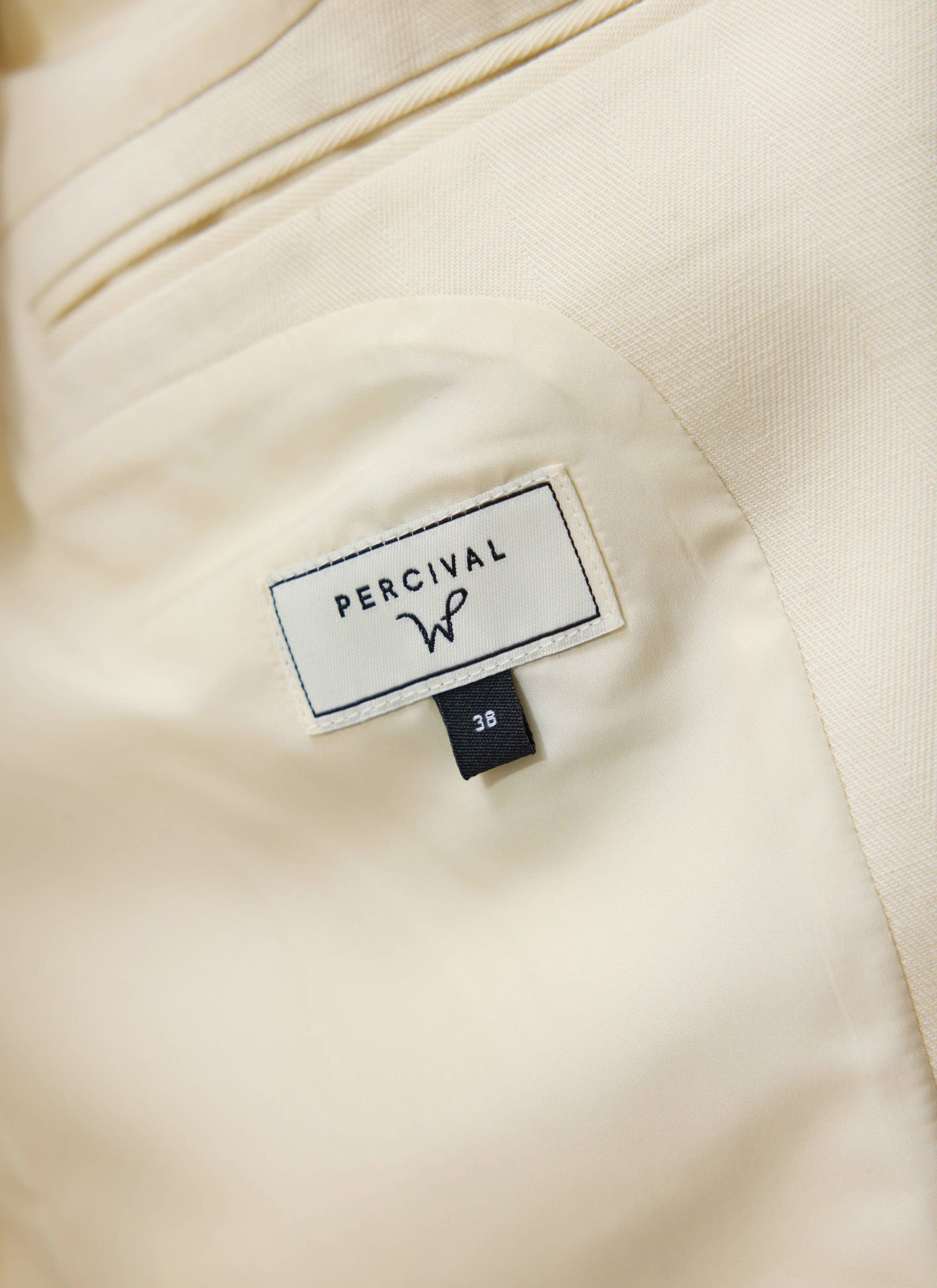 A close-up of the interior brand label of the Percival x Warren Alfie Baker tailored blazer in ecru.