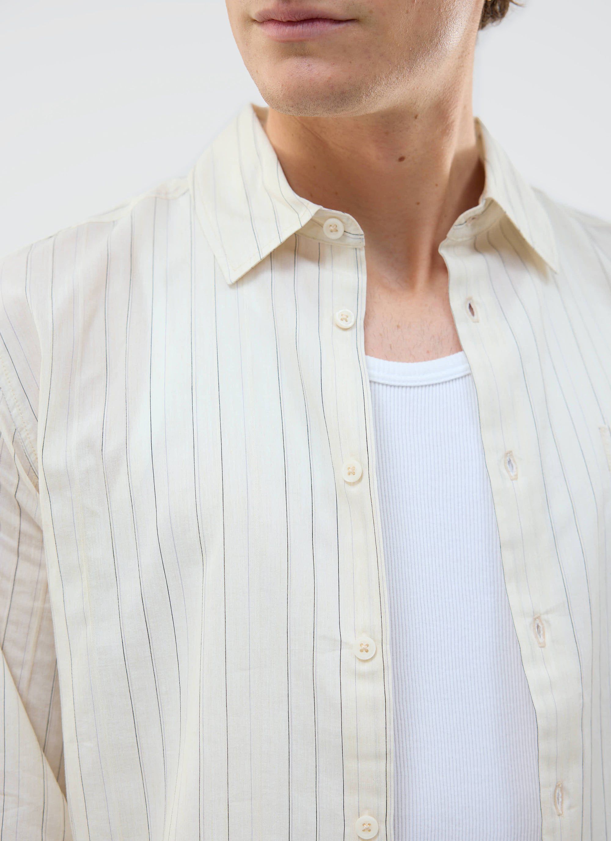 A close-up of a model wearing the ecru striped Lorenzo Pearce Shirt from Percival, styled over a white vest.