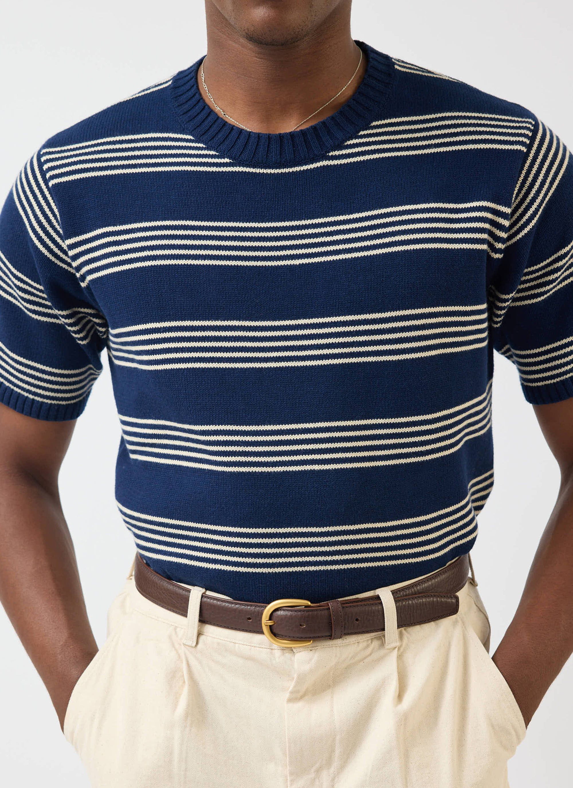 A close-up of a model wearing the Percival Fiction Knitted T-Shirt, a navy knit with fine off-white stripes.