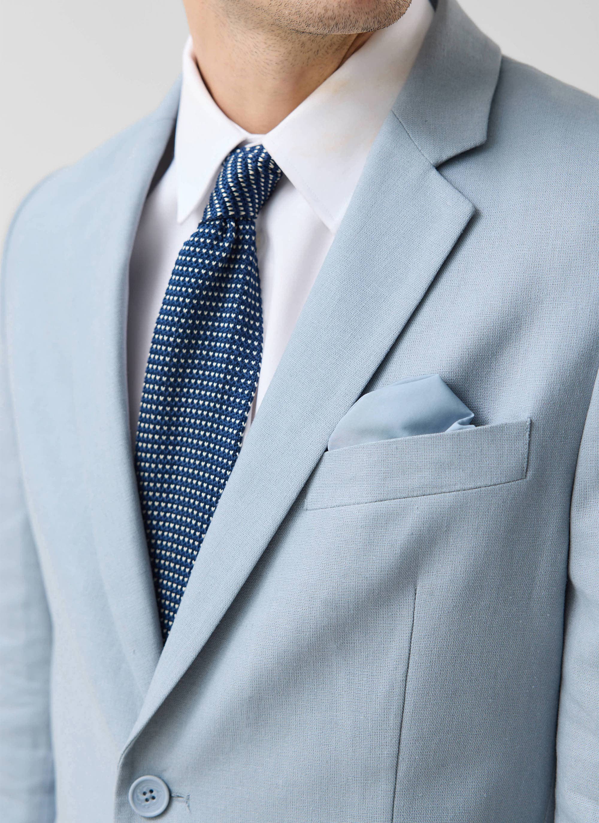 Close up of the Percival light blue tailored linen blazer with a white shirt and blue tie.
