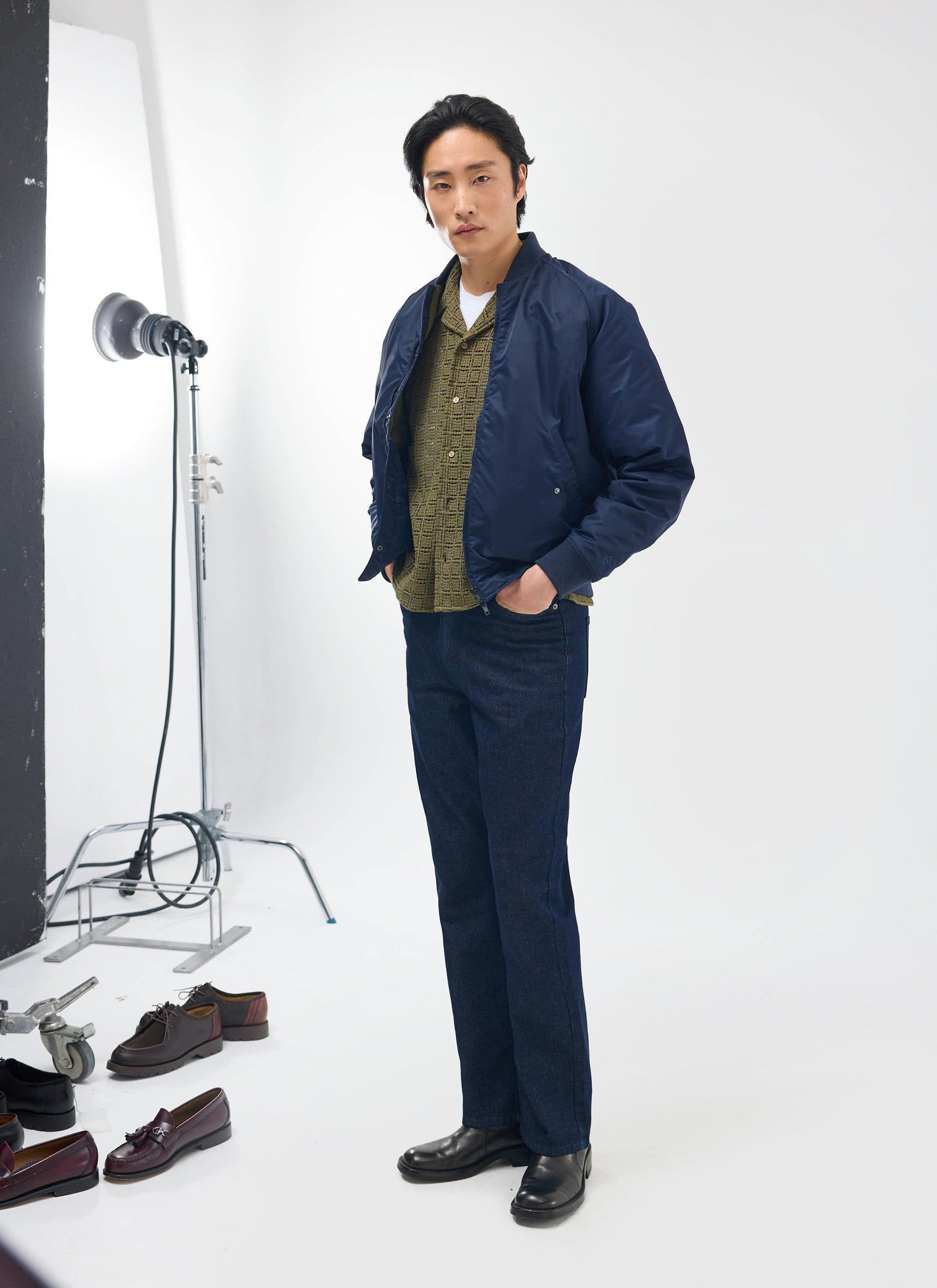 A male model wears the Percival Palermo Crochet Cuban Shirt in olive green, styled under a navy bomber jacket in a studio.