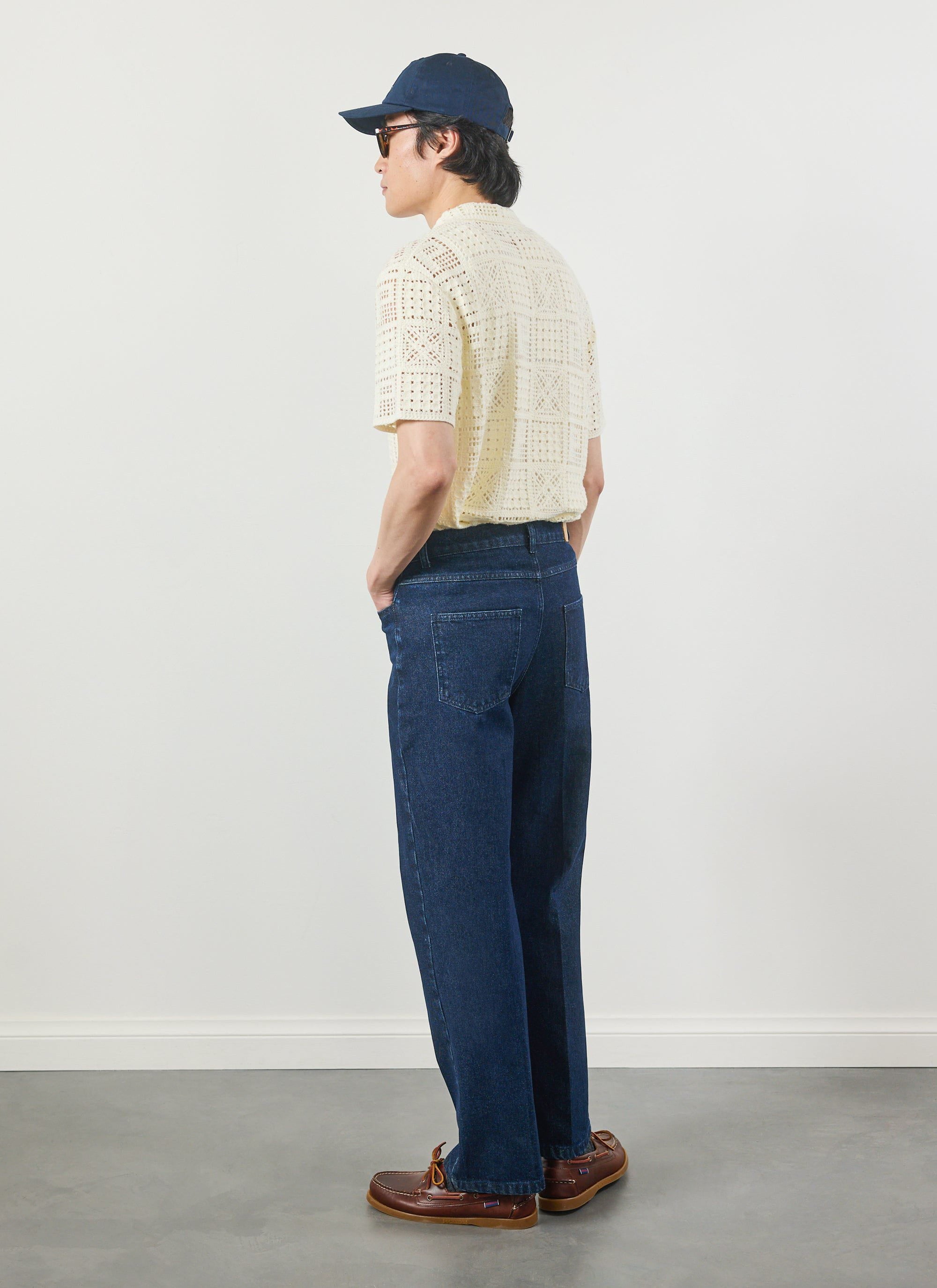 A model wearing the Percival Crochet Groundsman Shirt in ecru, styled with dark denim jeans and a cap, seen from behind.