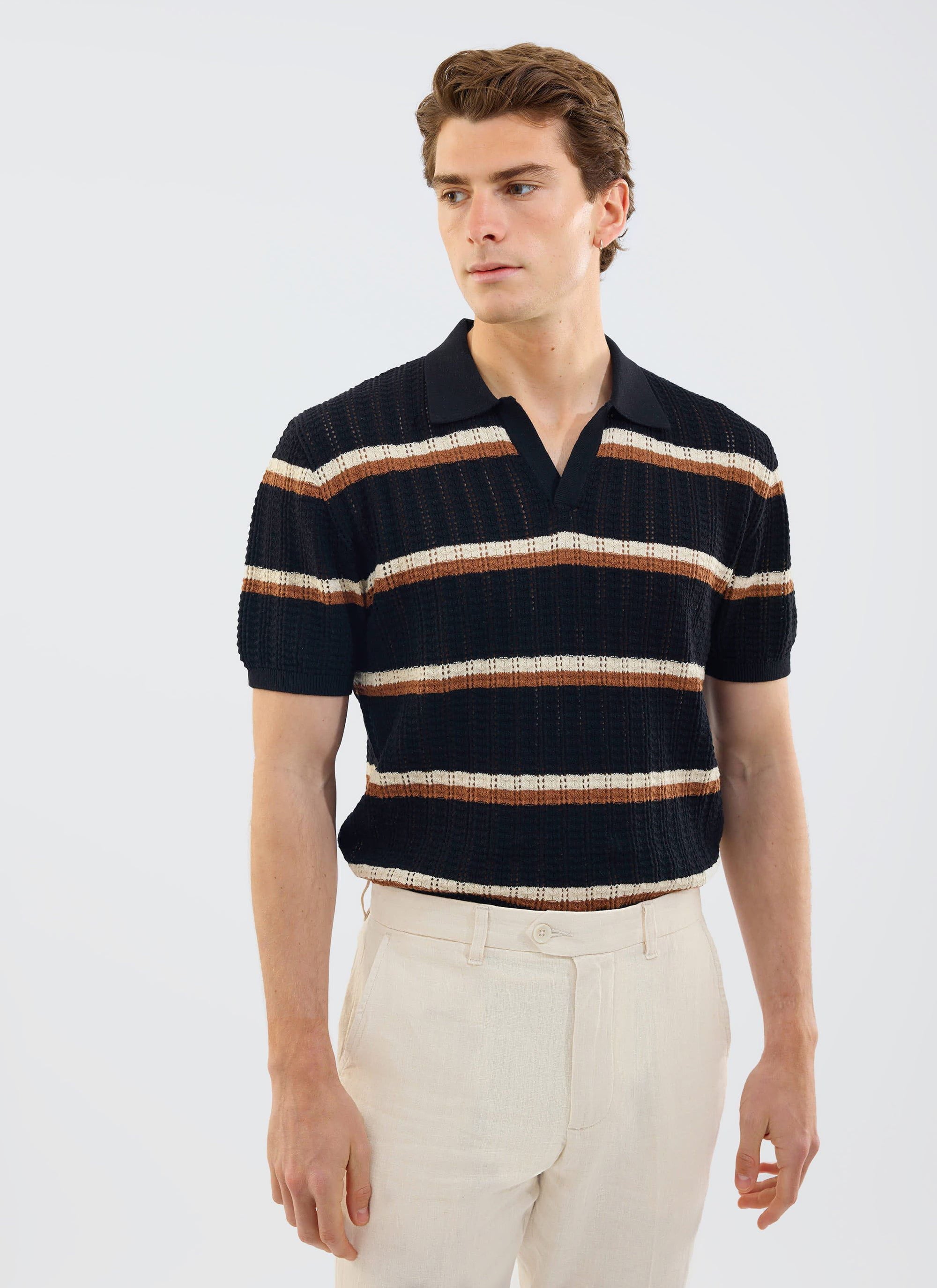 A model wears the Percival Tessaro Knitted Stripe Polo in black with cream and brown stripes, paired with cream trousers.