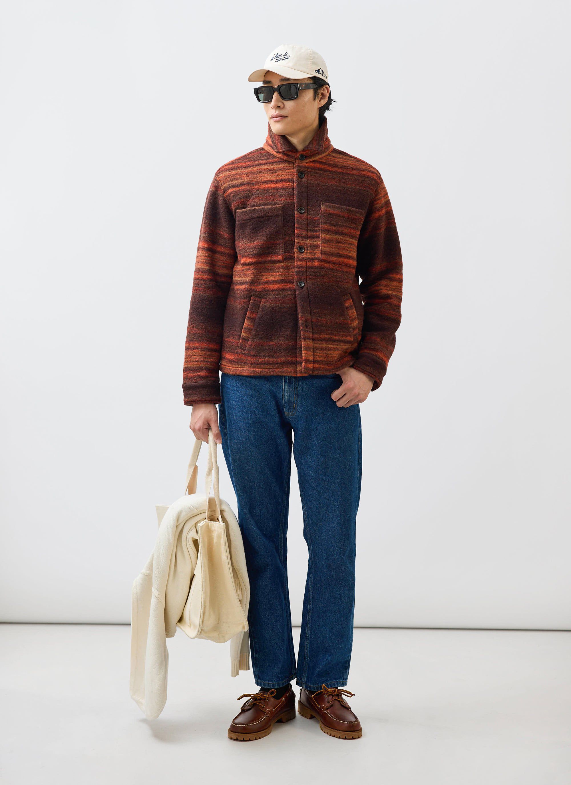 A man models the Percival Mississippi Jacquard Overshirt in burnt orange and brown, styled with blue jeans and sunglasses.