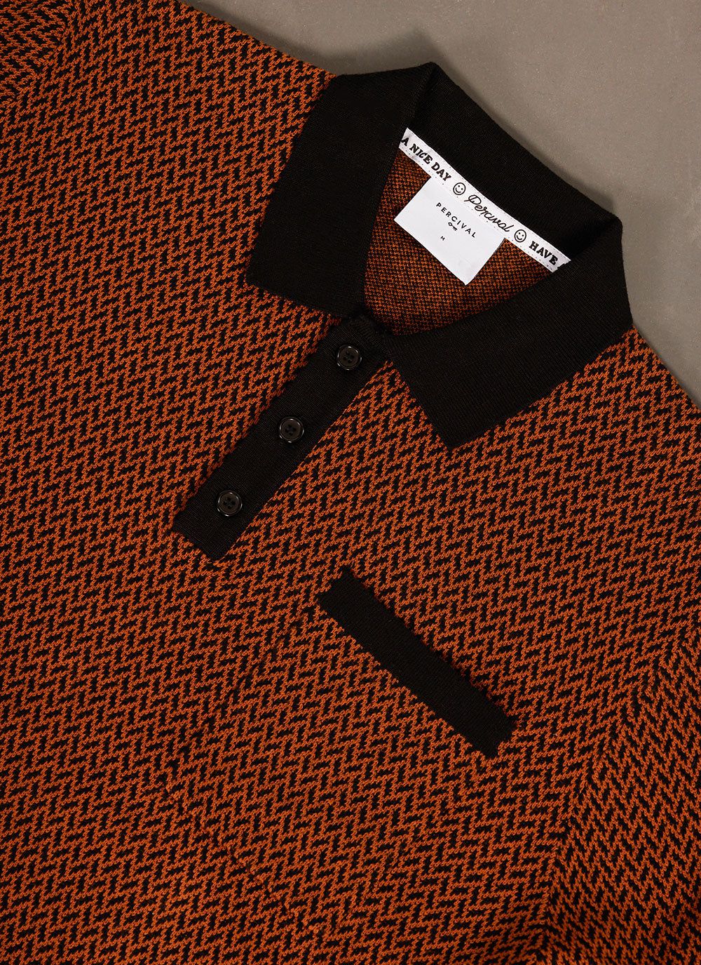 Close-up of the Percival Casa Martini Knitted Polo in espresso, a brown and black geometric knit with a black collar.
