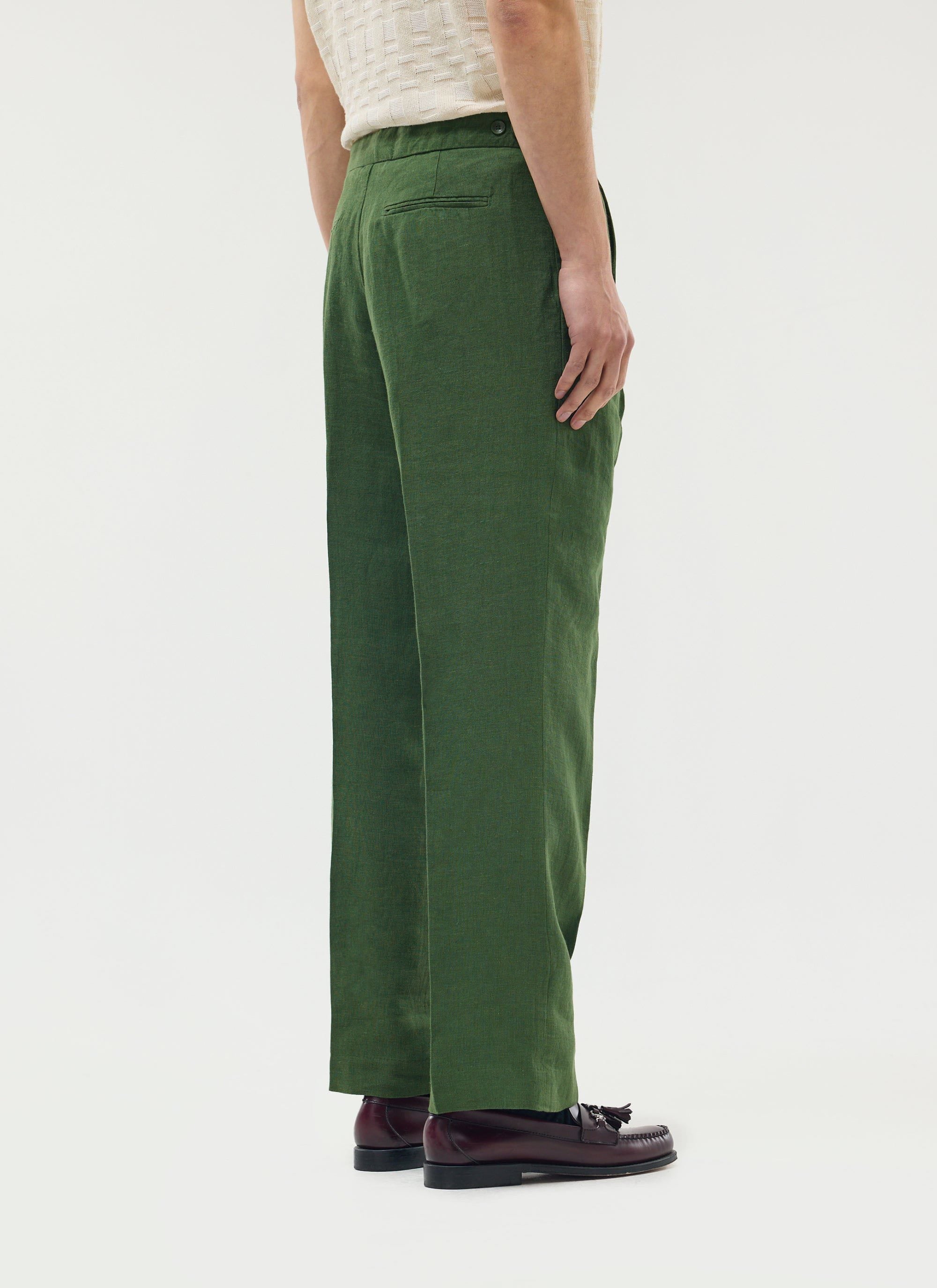 A model wears the Percival Pleated Tailored Trousers in Forest green linen, shot from behind on a white background.