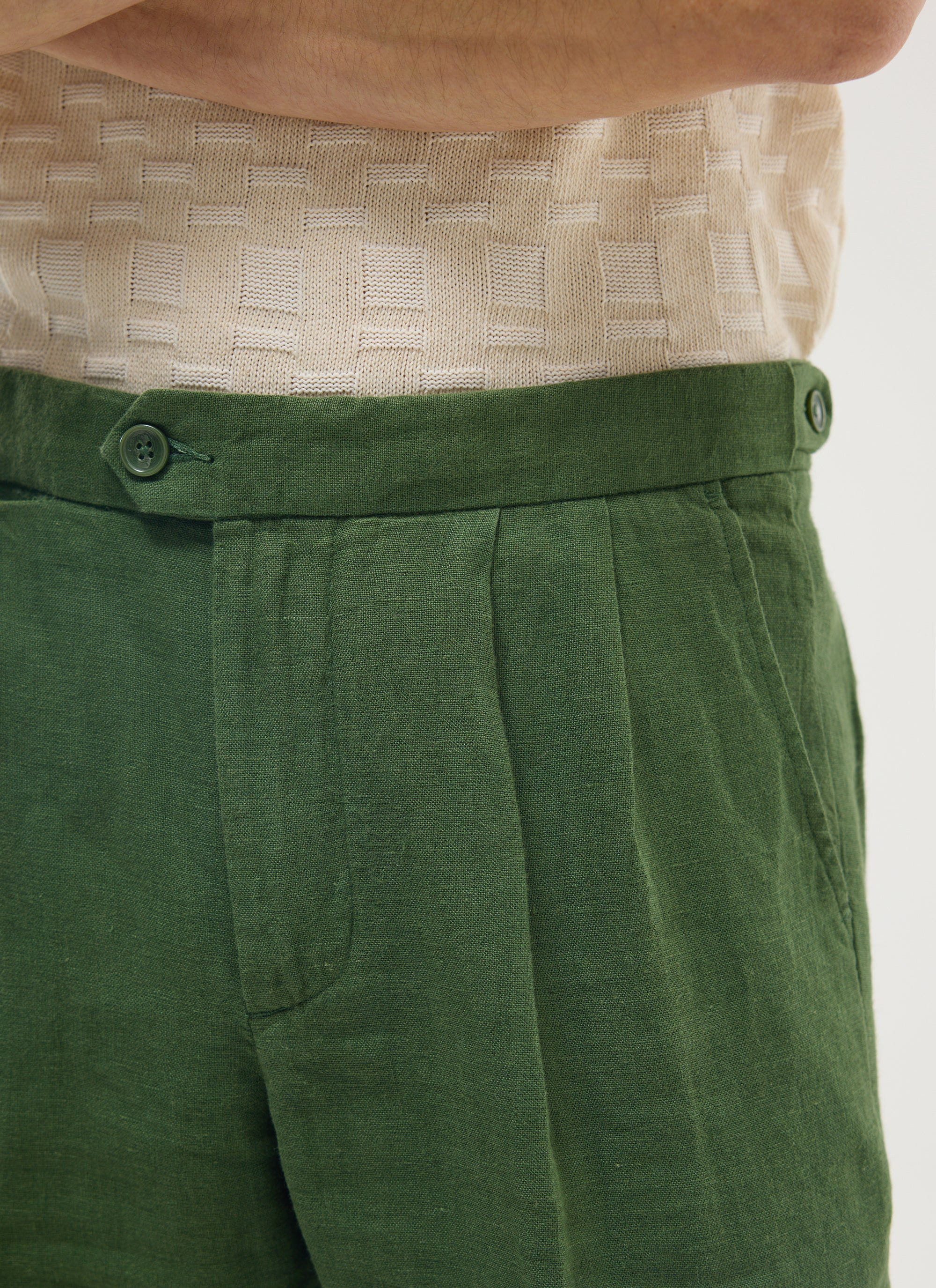 Close up of the waistband and pleat on the Percival forest green linen tailored trousers, worn with a cream knit top.