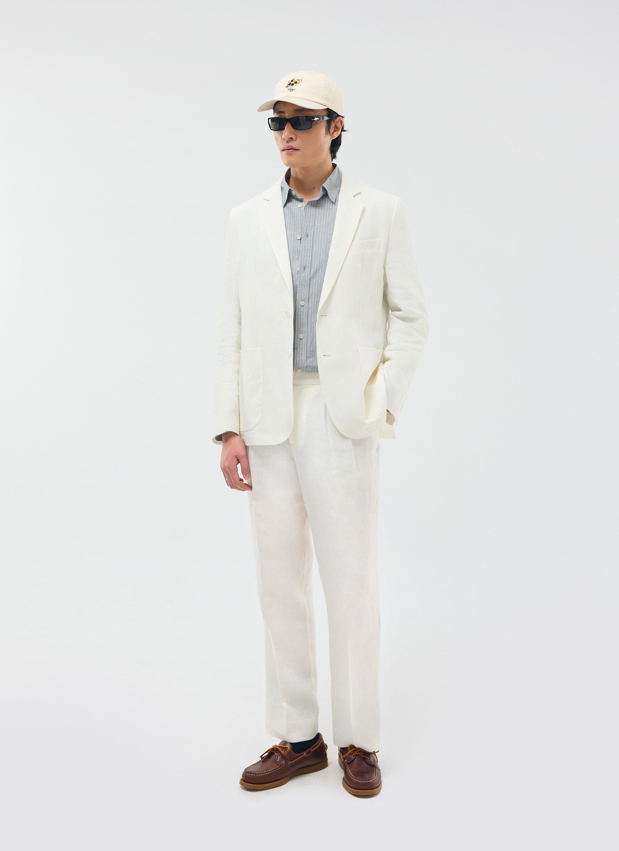 A model wears the white Percival Relaxed Tailored Linen Blazer with matching trousers, a striped shirt, and sunglasses.