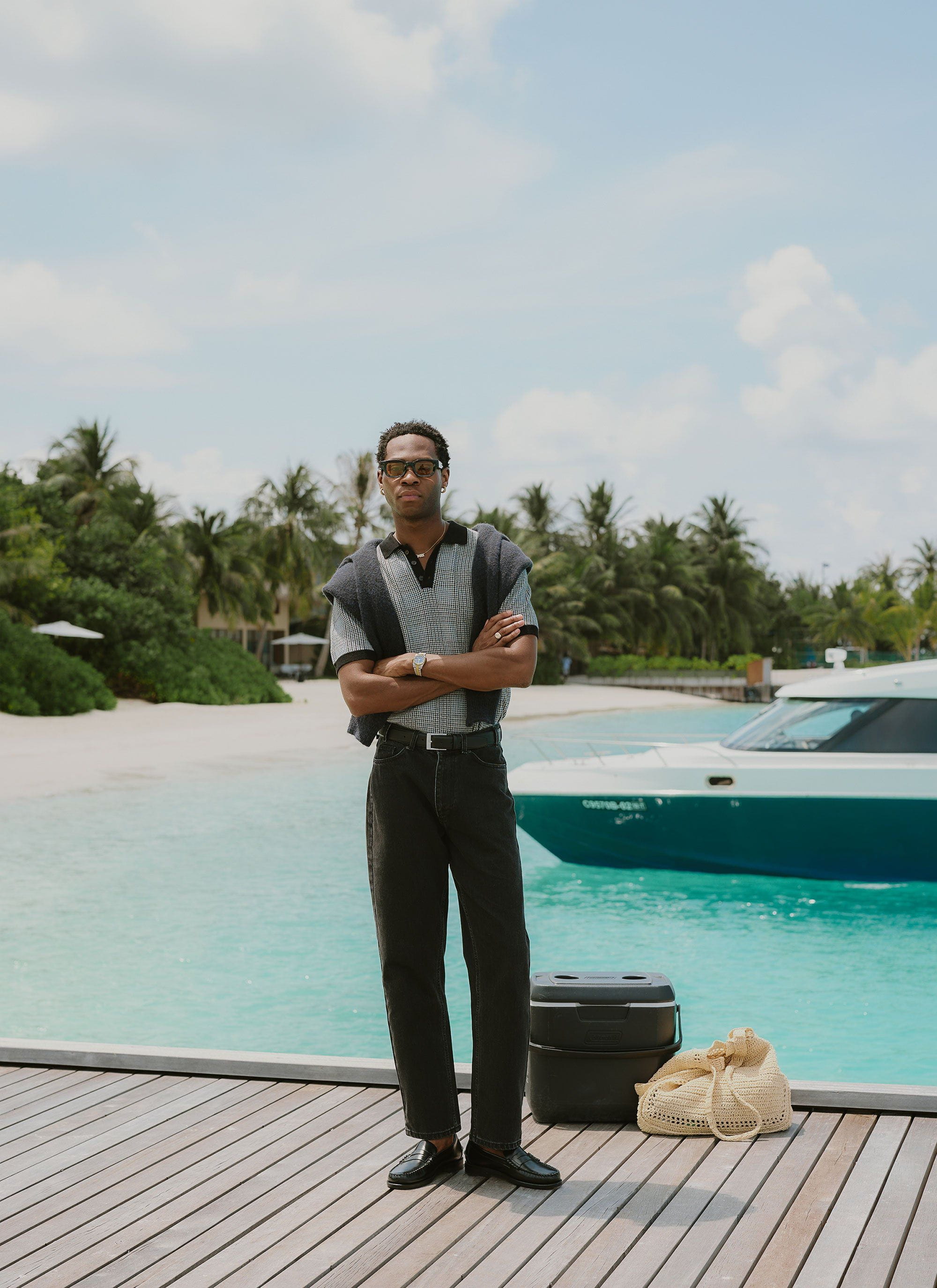 A man models the Percival Casa Martini Knitted Polo in navy puppytooth on a dock by the sea.