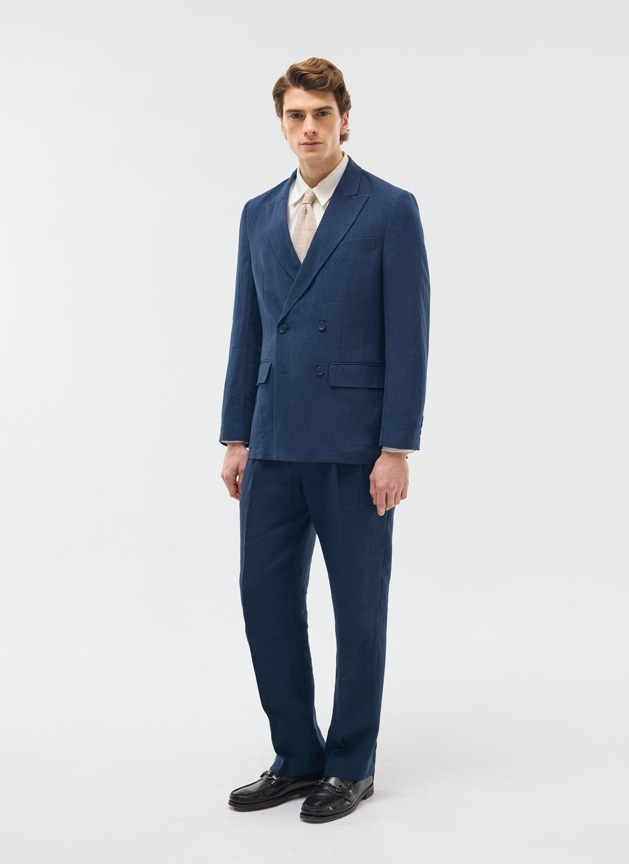 A model wears the Percival navy linen double breasted blazer with matching trousers, a cream shirt, and tie.