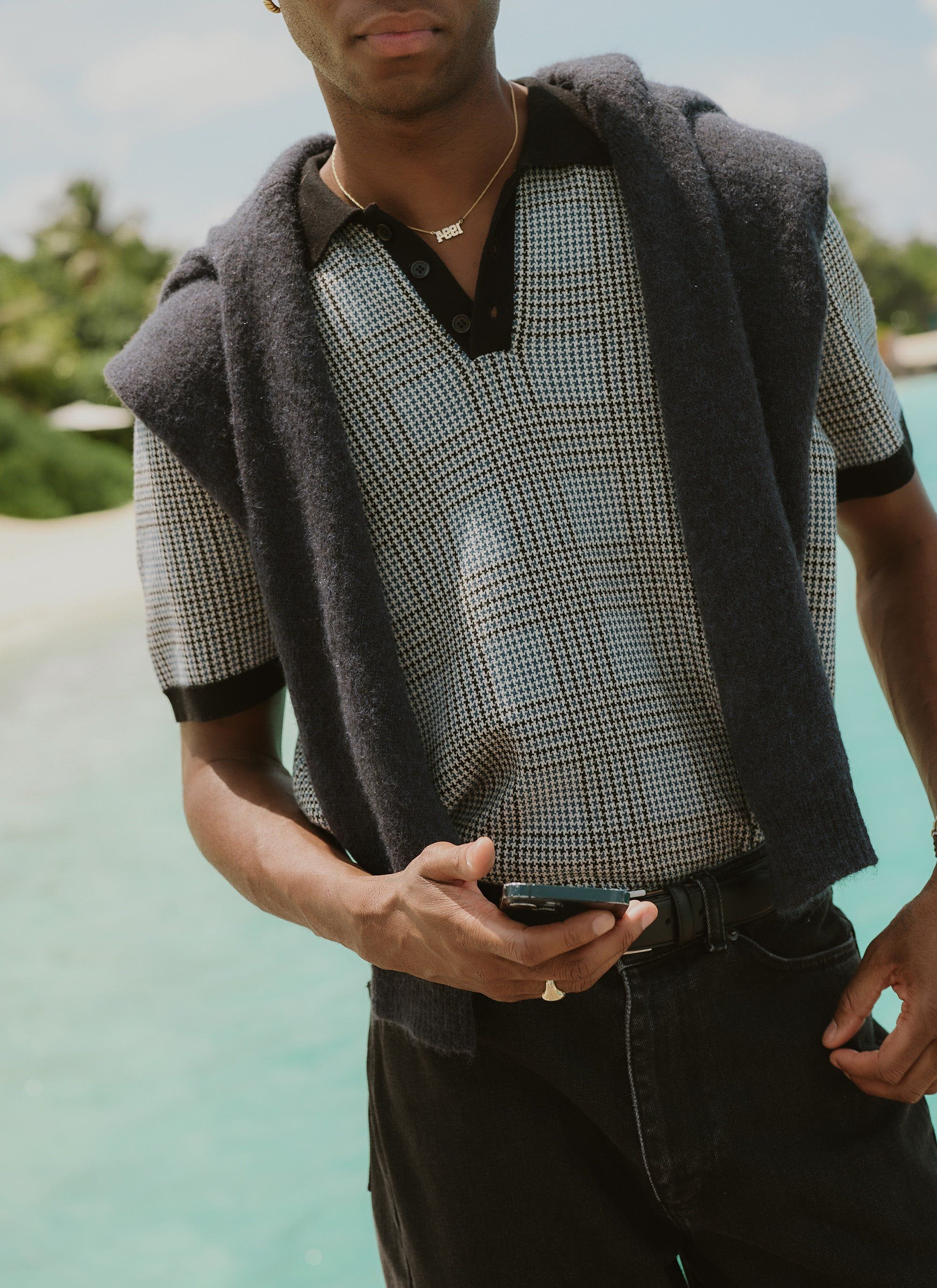 A man models the Percival Casa Martini Knitted Polo in navy puppytooth, with a navy jumper over his shoulders.