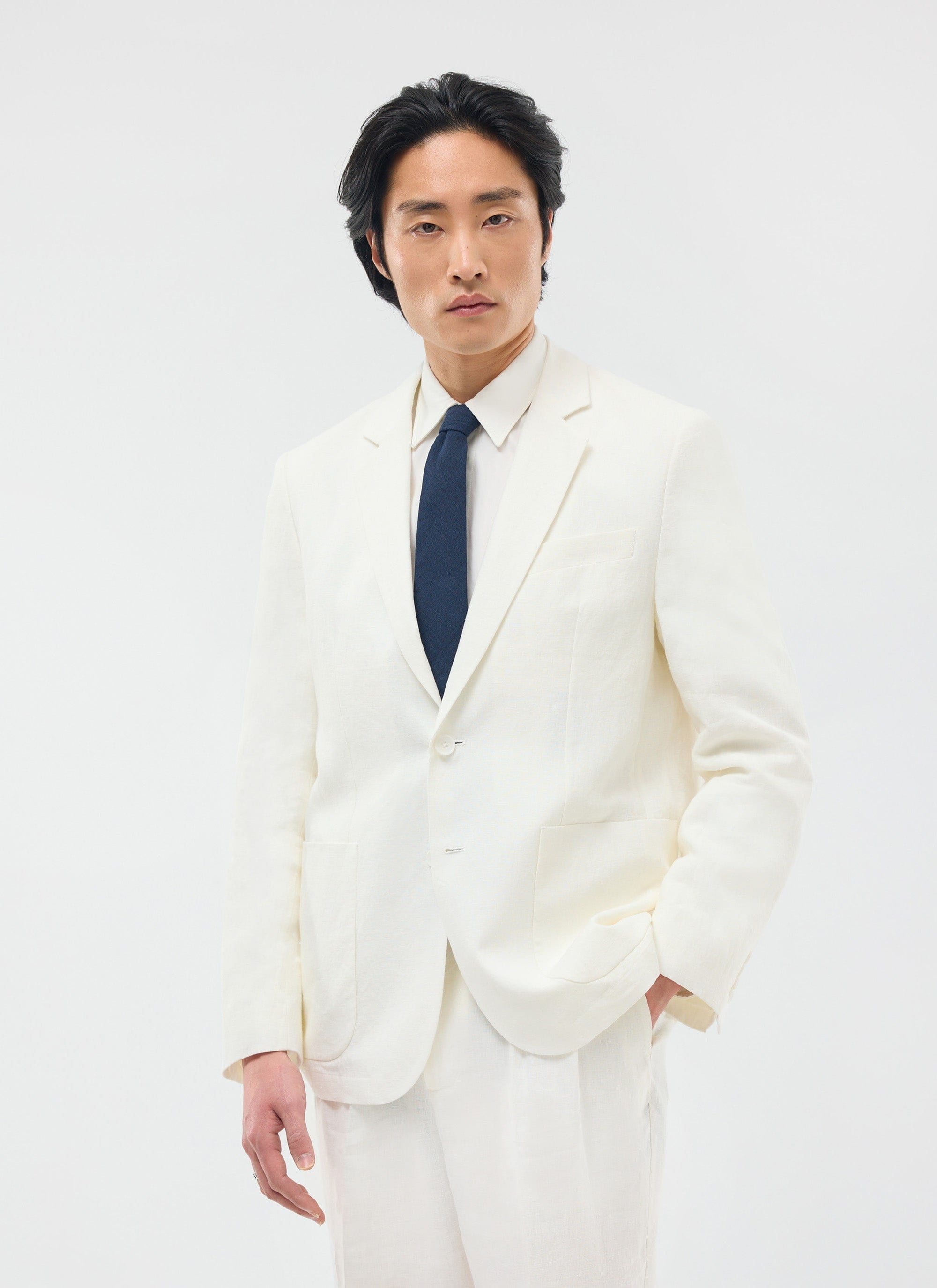 A model wears the Percival Relaxed Tailored Linen Blazer in white, styled with a white shirt and navy tie.