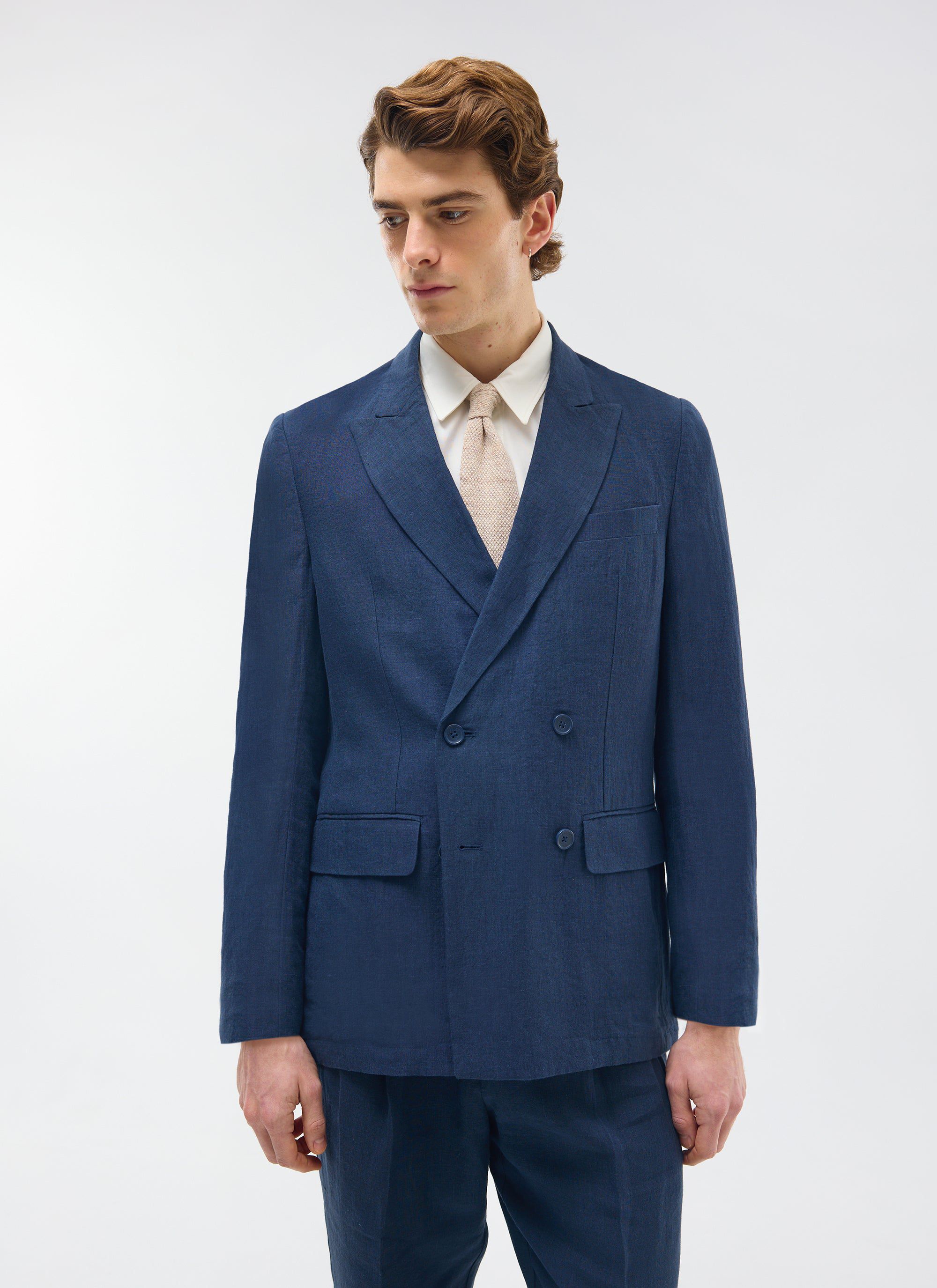 A model wears the full Percival navy linen suit, featuring the double-breasted blazer, with a white shirt and cream tie.