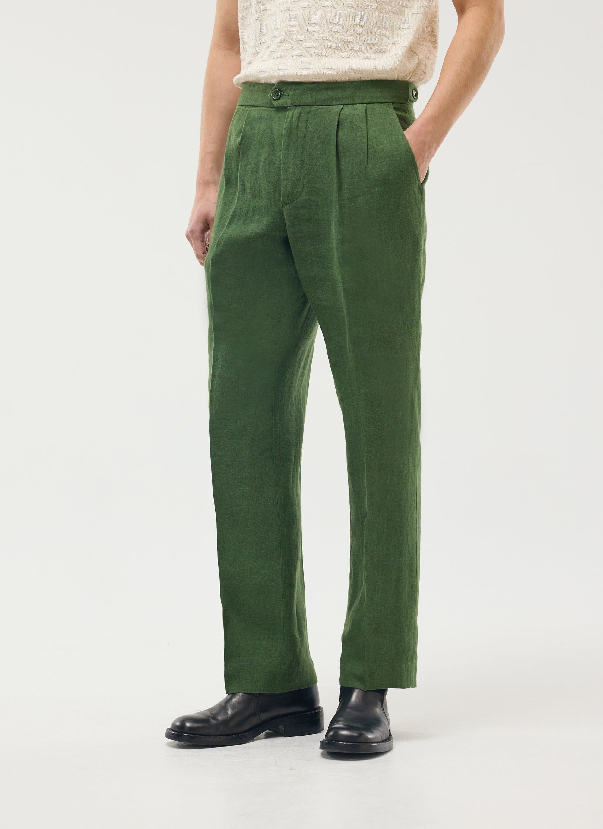 A model wears Percival's forest green linen Pleated Tailored Trousers with a cream textured top and black leather boots.
