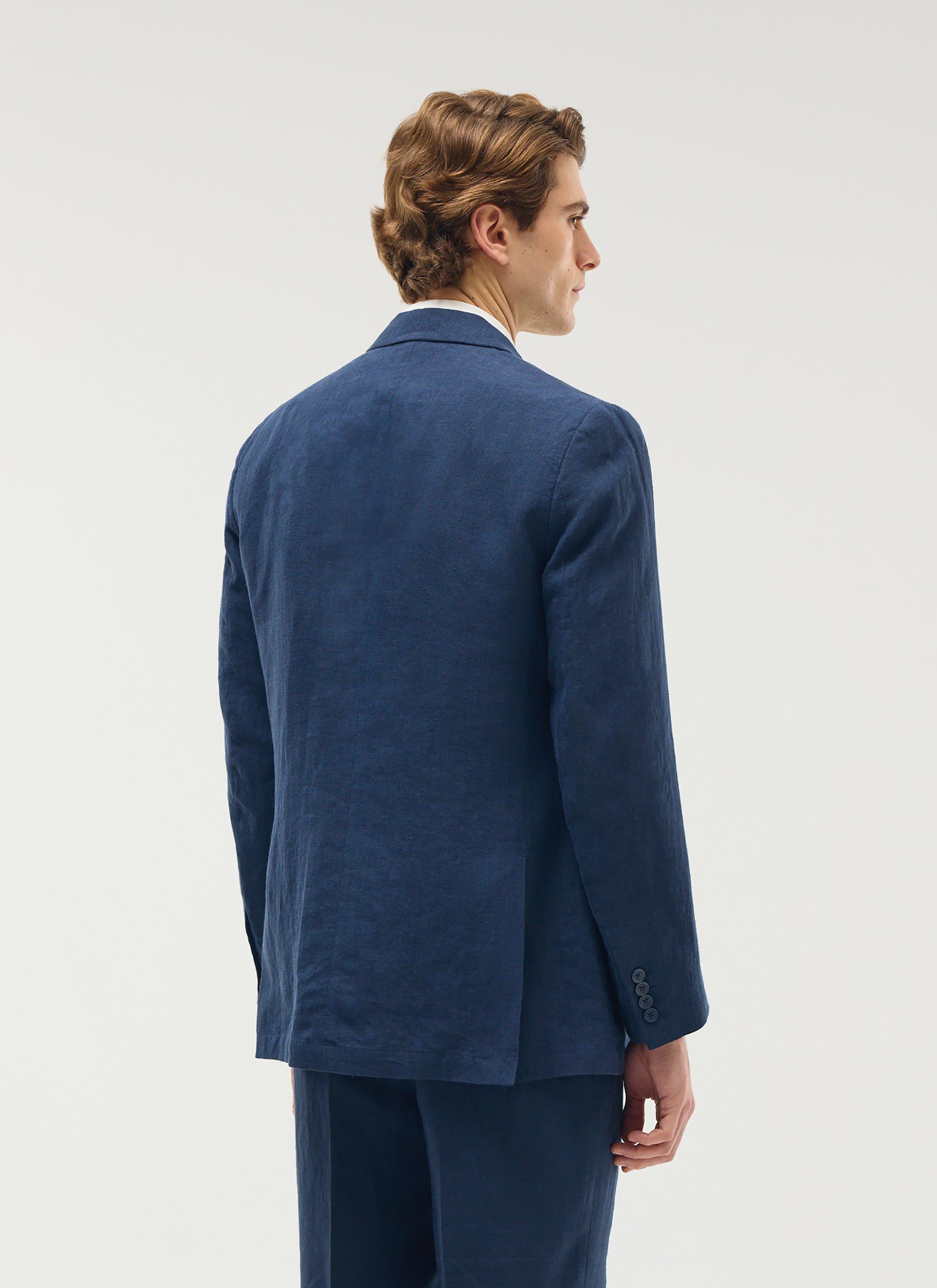 Back view of a model wearing the Percival tailored double breasted linen blazer in navy.