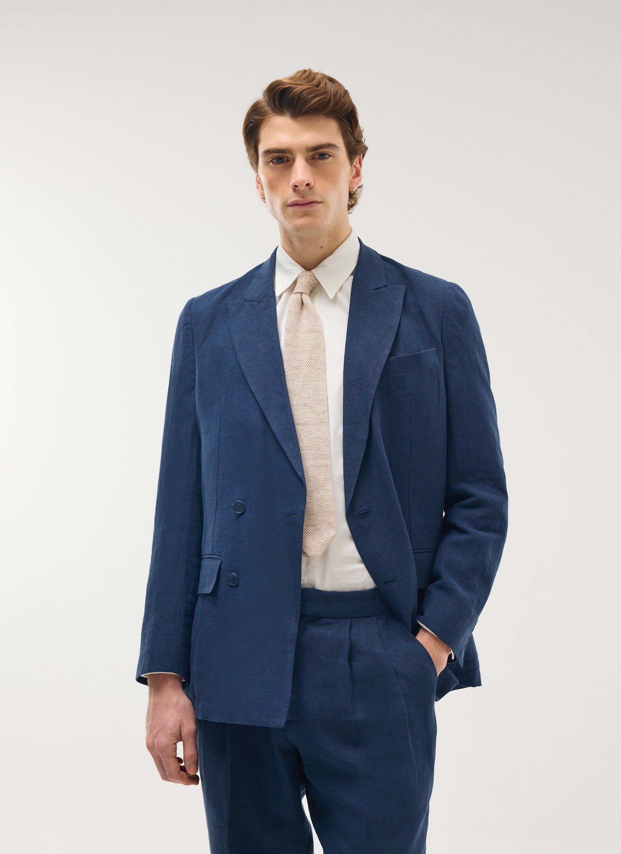 Model wears the Percival navy linen double-breasted blazer and matching trousers with a white shirt and light tie.