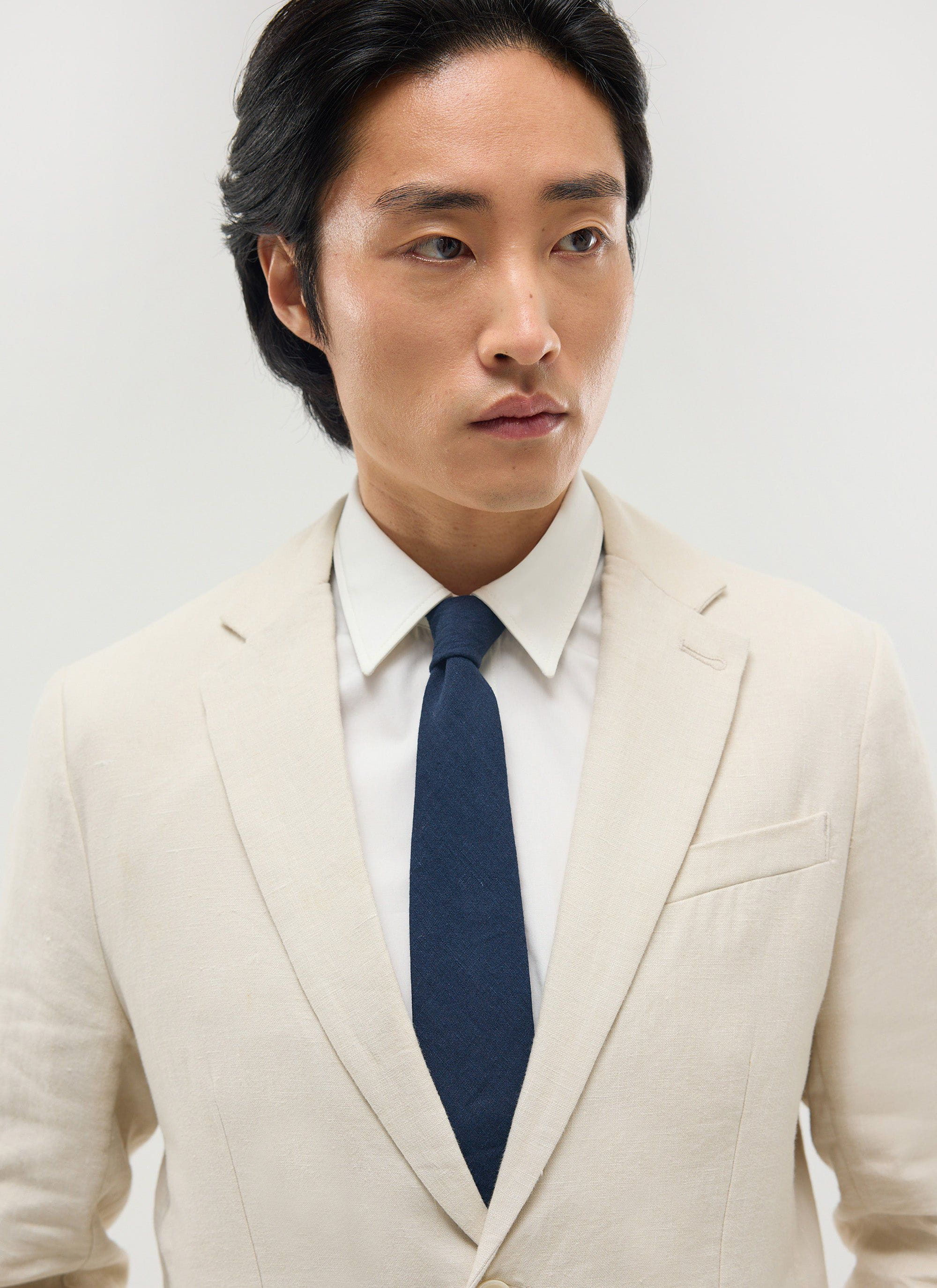 Close up of a model wearing the Percival navy linen tie with a cream linen suit jacket and white shirt.