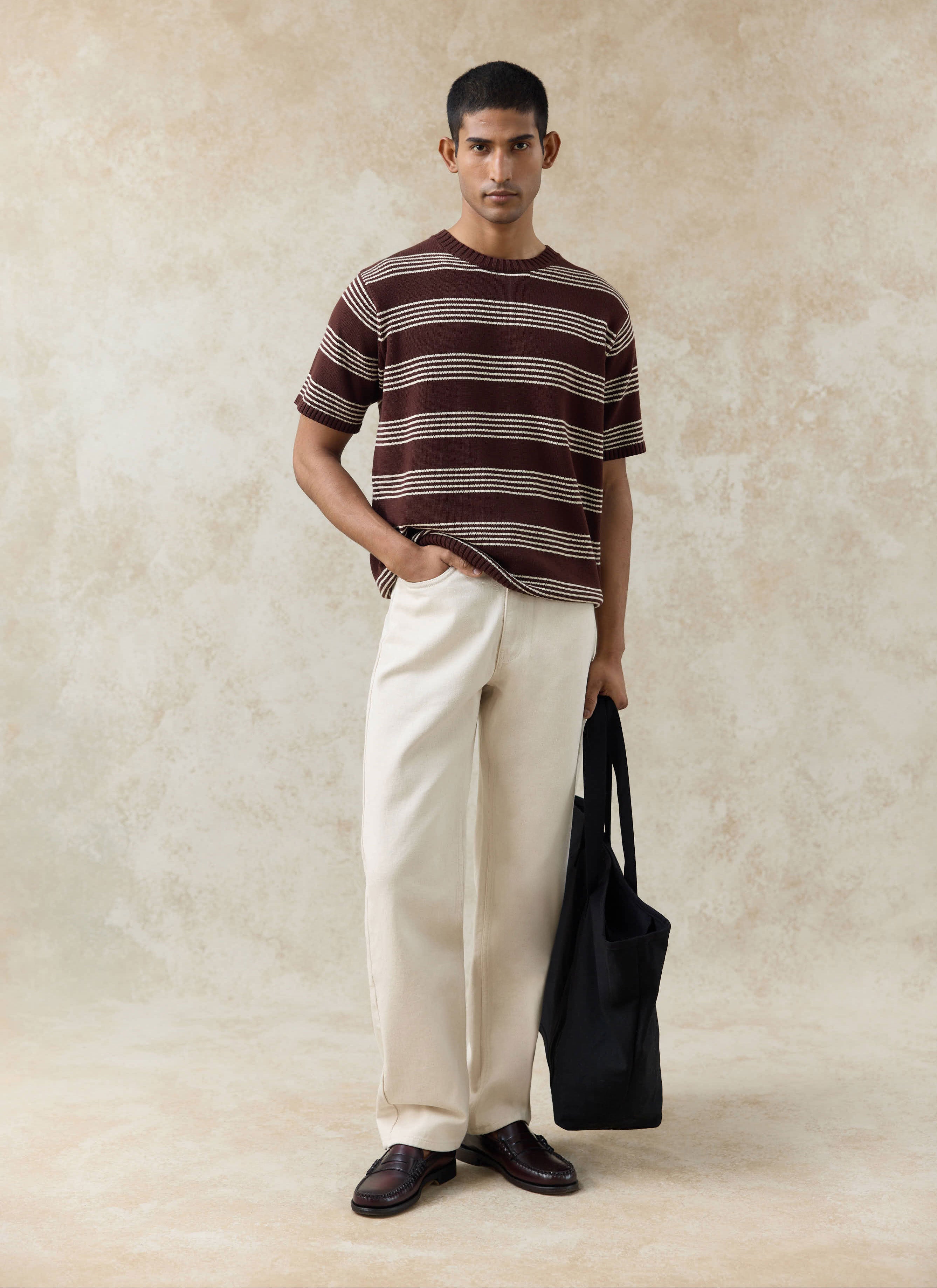 The Percival Fiction Striped Knitted T Shirt in espresso brown, styled with cream trousers and a black tote bag.