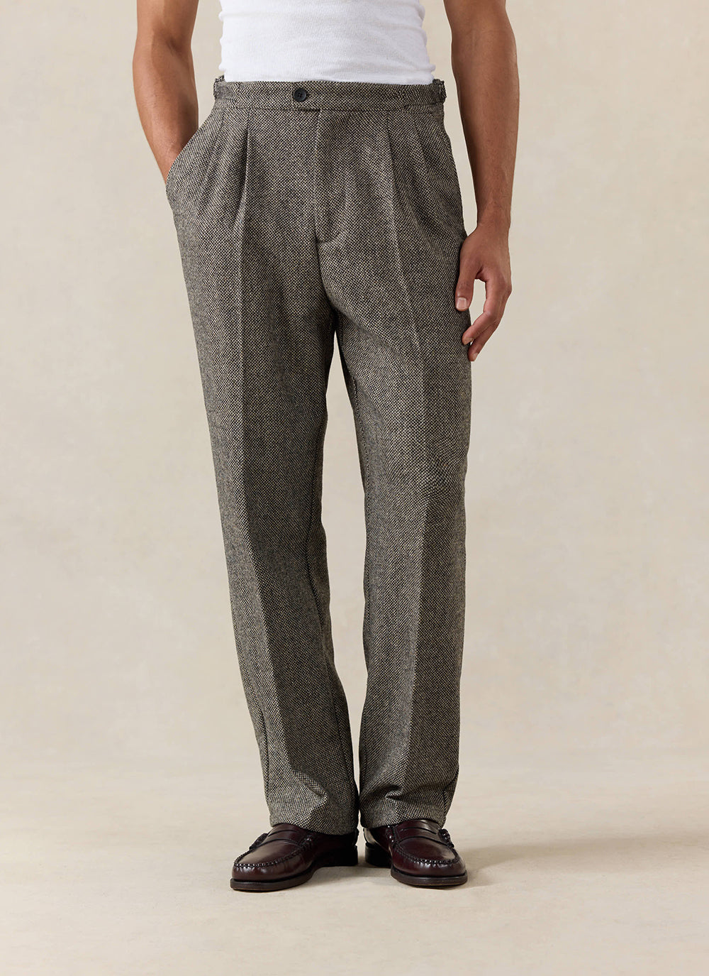 A model wears the Percival Blake Double Pleated Tailored Trousers in Grey Birdseye Wool.
