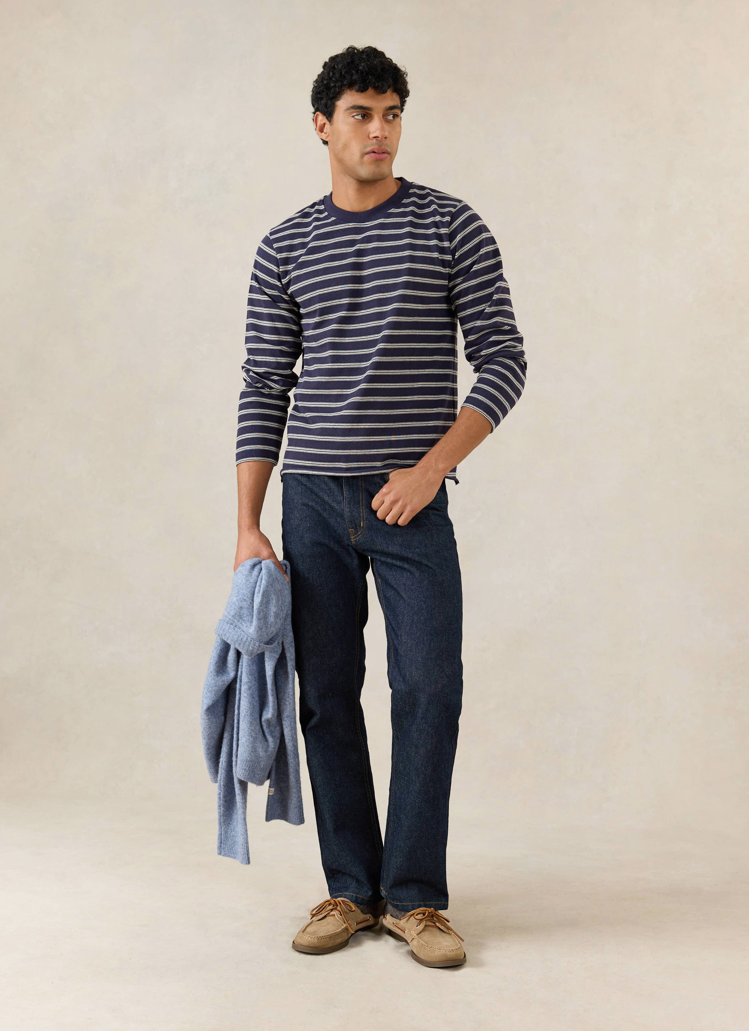 Model wears the Percival Arlo raw hem long sleeve Breton t-shirt in navy stripe, with dark denim and tan shoes.